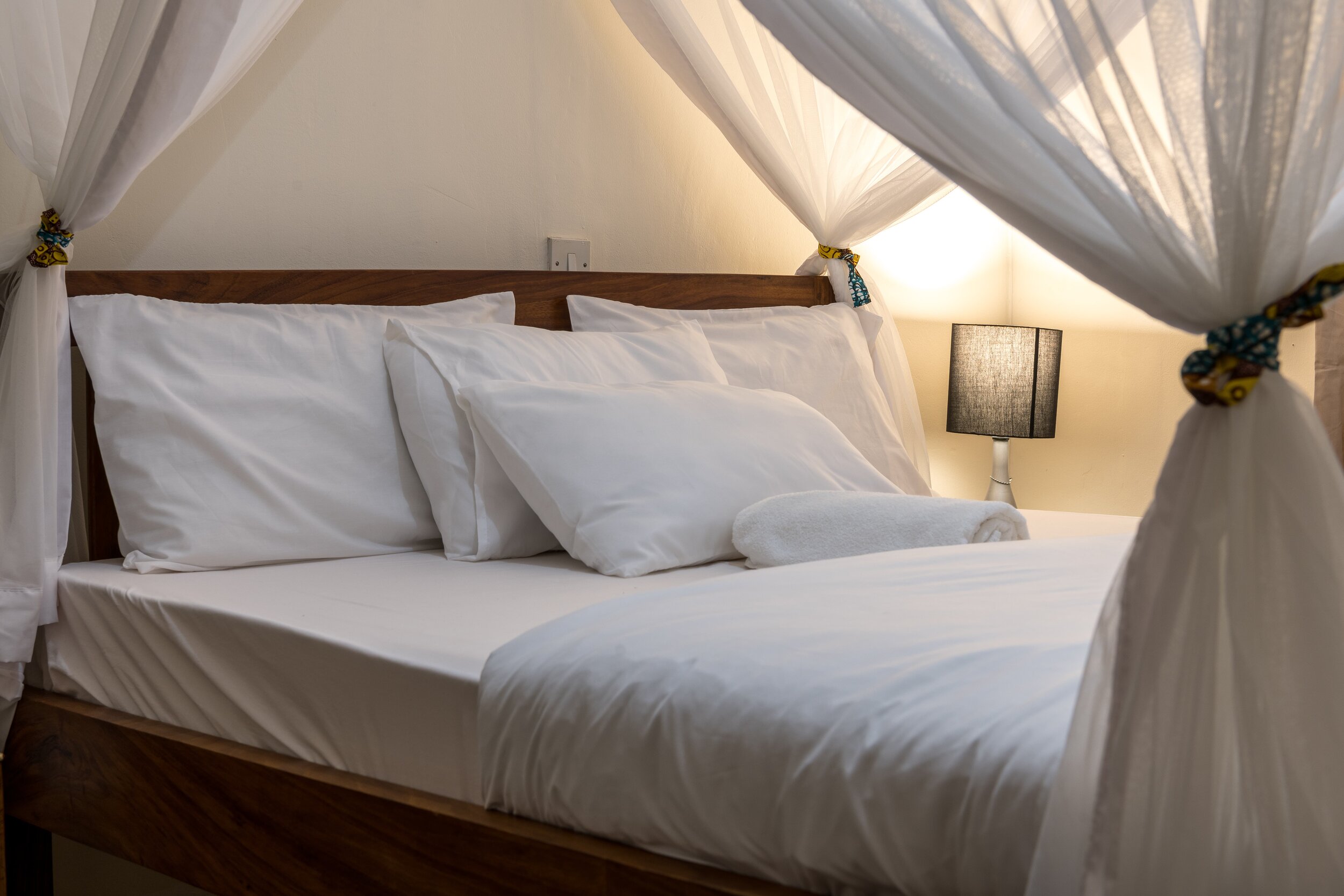 Guesthouse bed and breakfast accommodation with wooden king size bed, white bed linen, mosquito net and bedside lamp