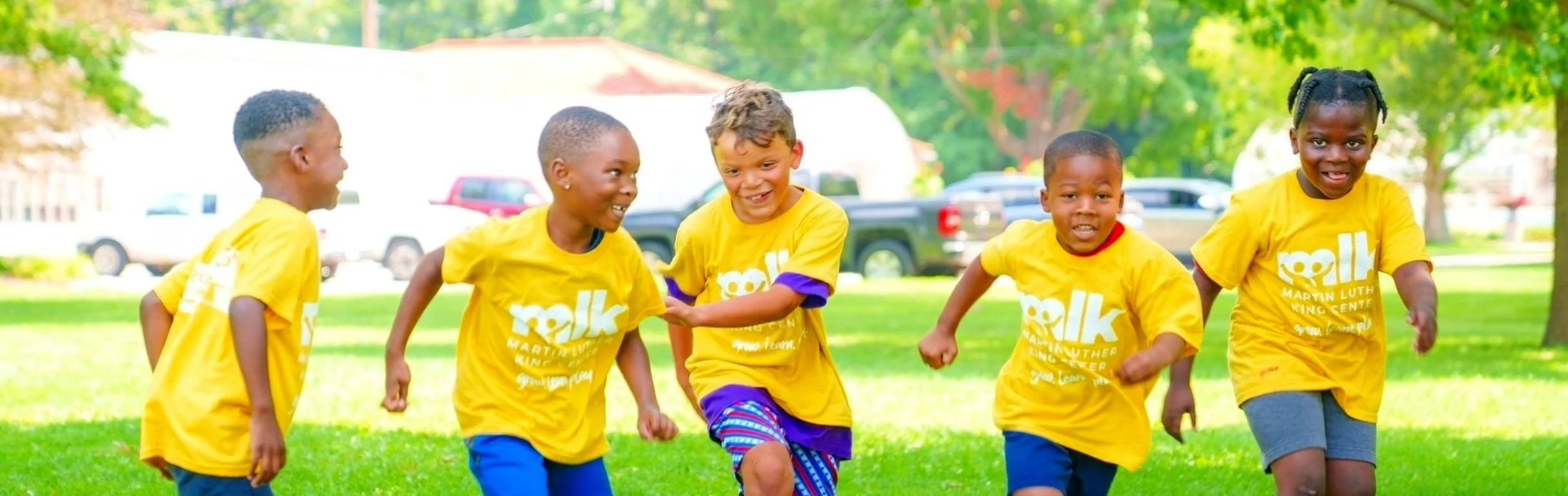 Group of children wearing yellow Martin Luther King Center shirts playing outdoors on grass