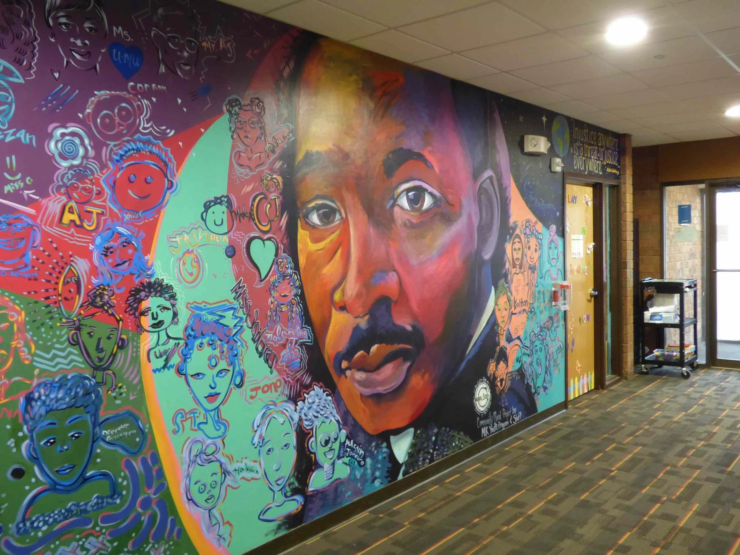 Colorful mural featuring a portrait of a man, surrounded by vibrant abstract designs and various doodles on a hallway wall.