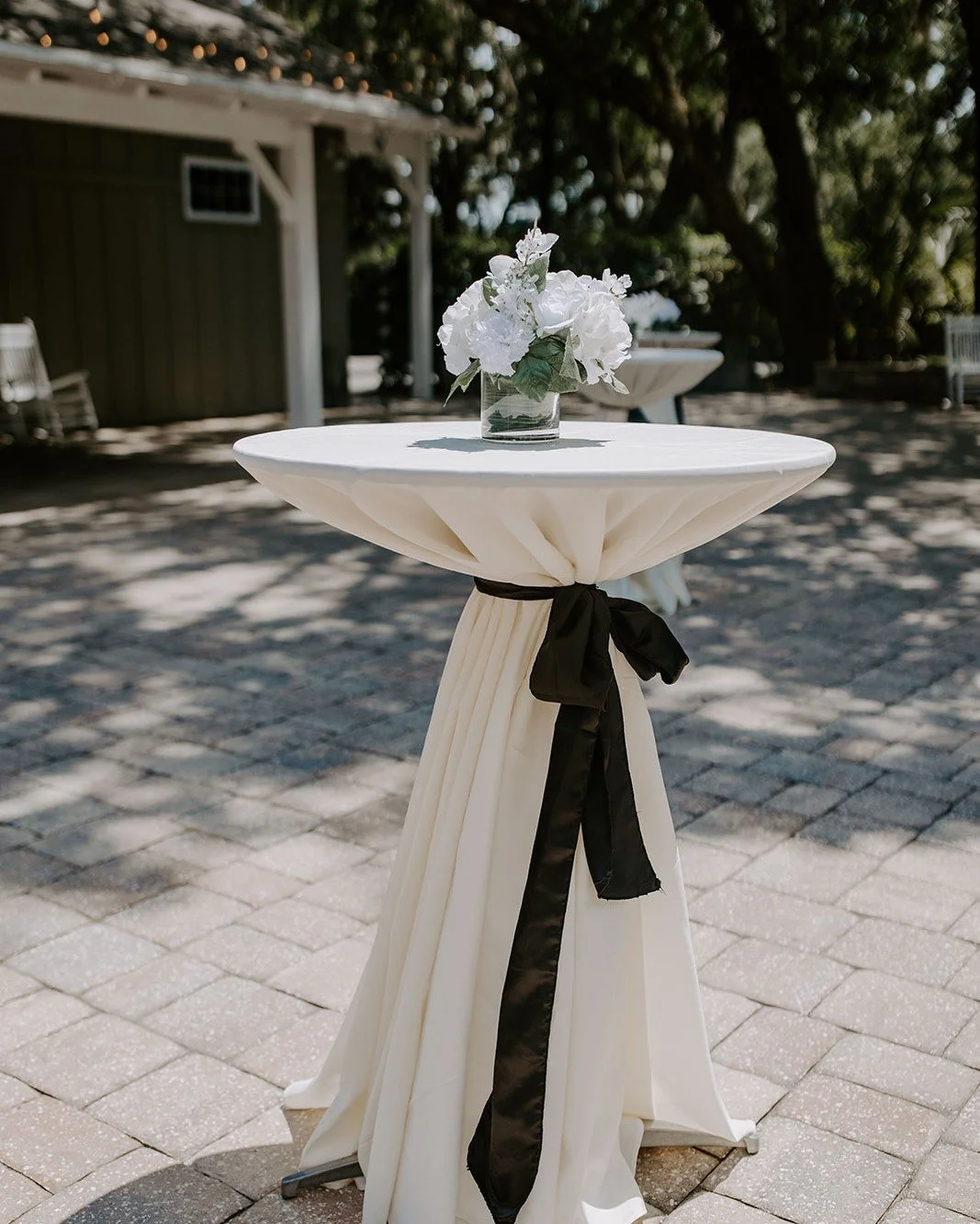 Cocktail hour sets the tone for the celebration to come.

As guests gather beneath the oak trees, every detail helps create an atmosphere that's both welcoming and unforgettable. Crisp white linens, classic black tie accents, and fresh white florals 