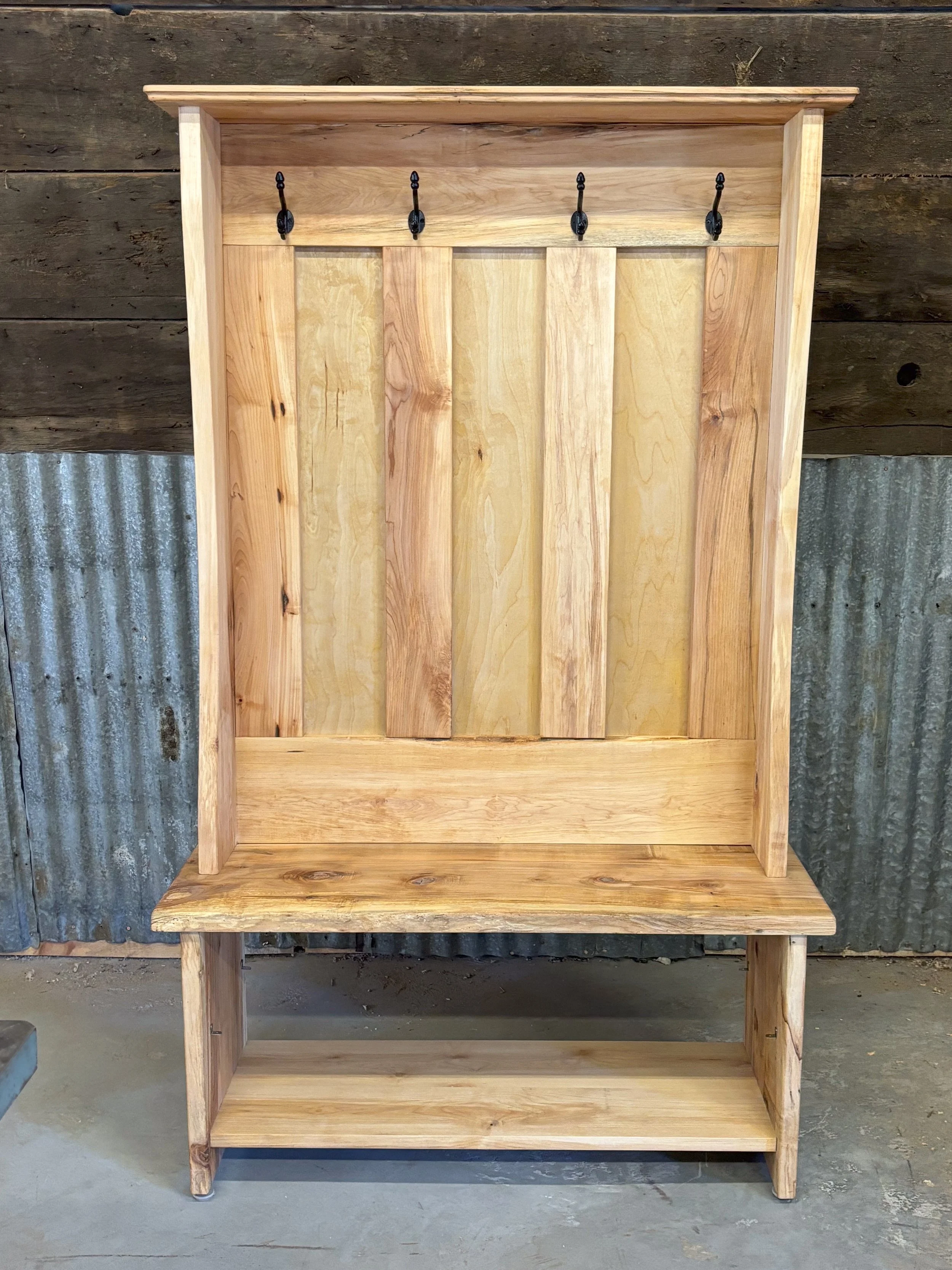 Wooden hall tree with hooks for hanging items, a bench seat, and a lower shelf, set against a rustic wall.