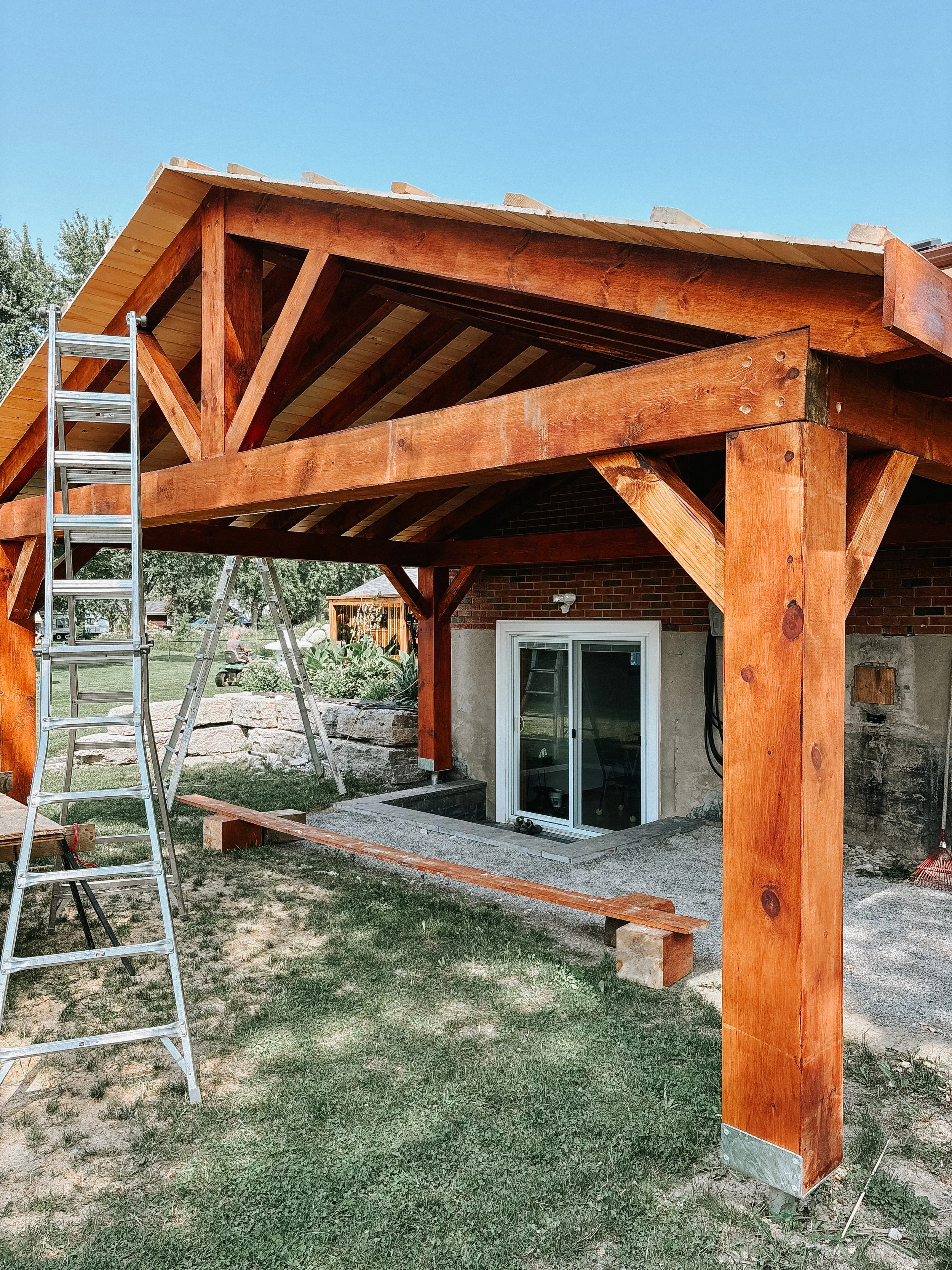 Wooden patio cover under construction with ladders and tools in backyard.
