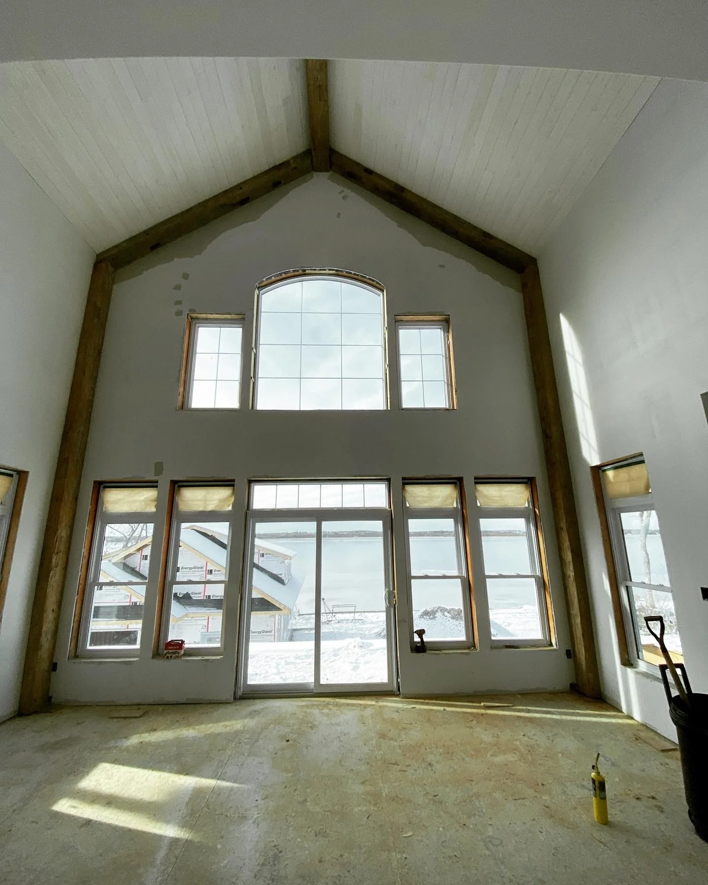 Interior of a house under construction with large windows overlooking a snowy landscape.