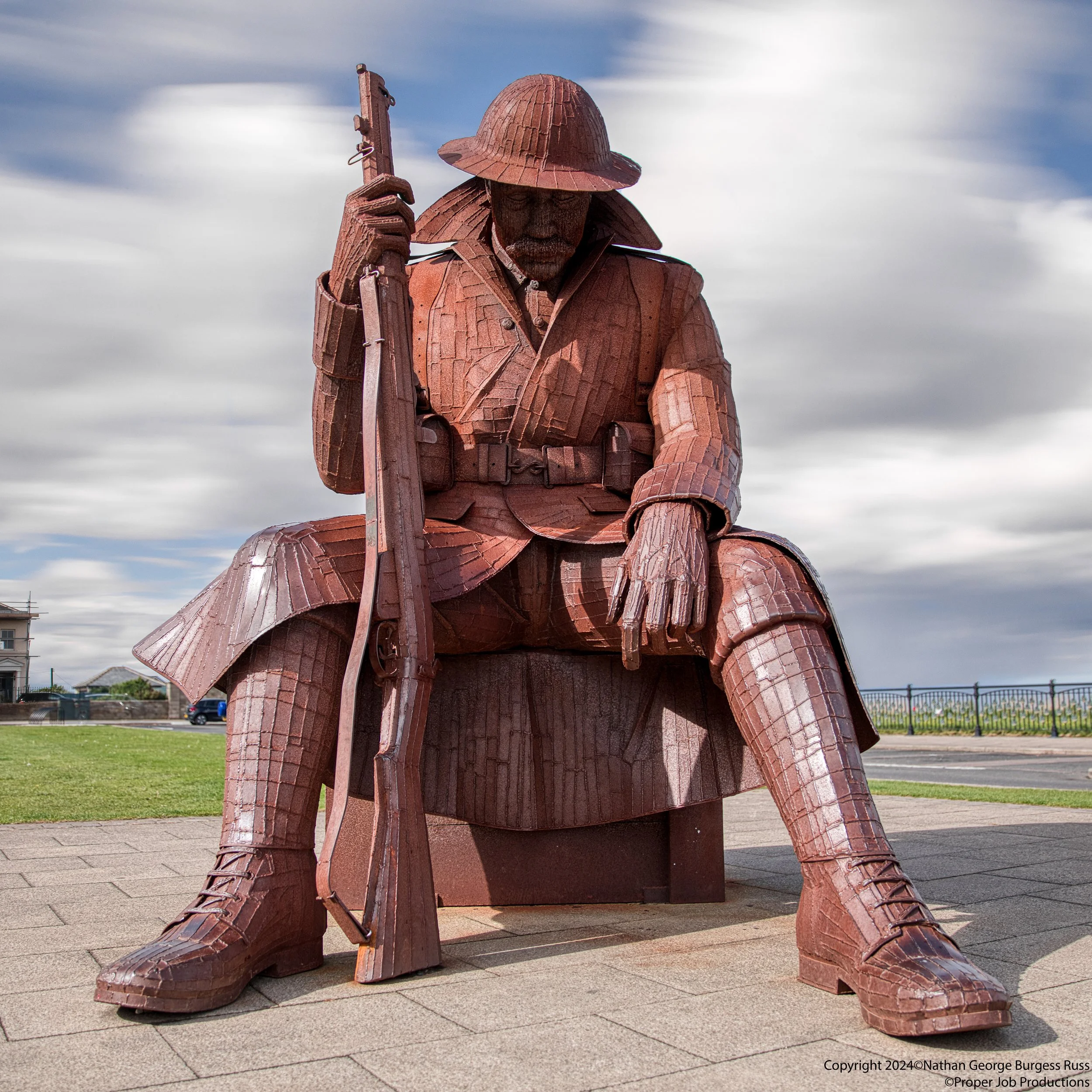 Tommy by Ray Lonsdale, and is built from corten steel, which gives it the rusty red appearance.  

Tommy was officially commissioned as 1101 or (Eleven-O-One), but everyone calls the statue Tommy because it resembles the stereotypical Tommy.

This st