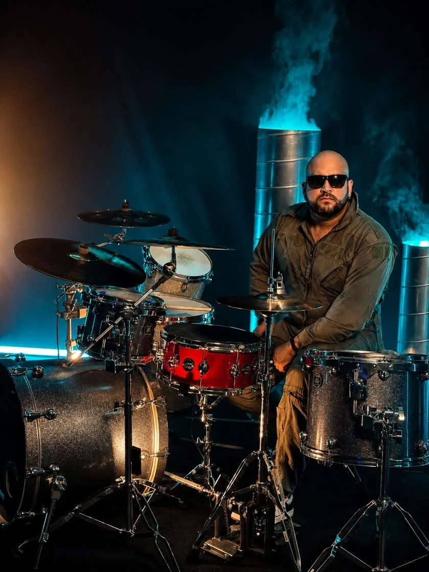 PH Teixeira seated at a full drum kit in a dramatic blue-lit studio