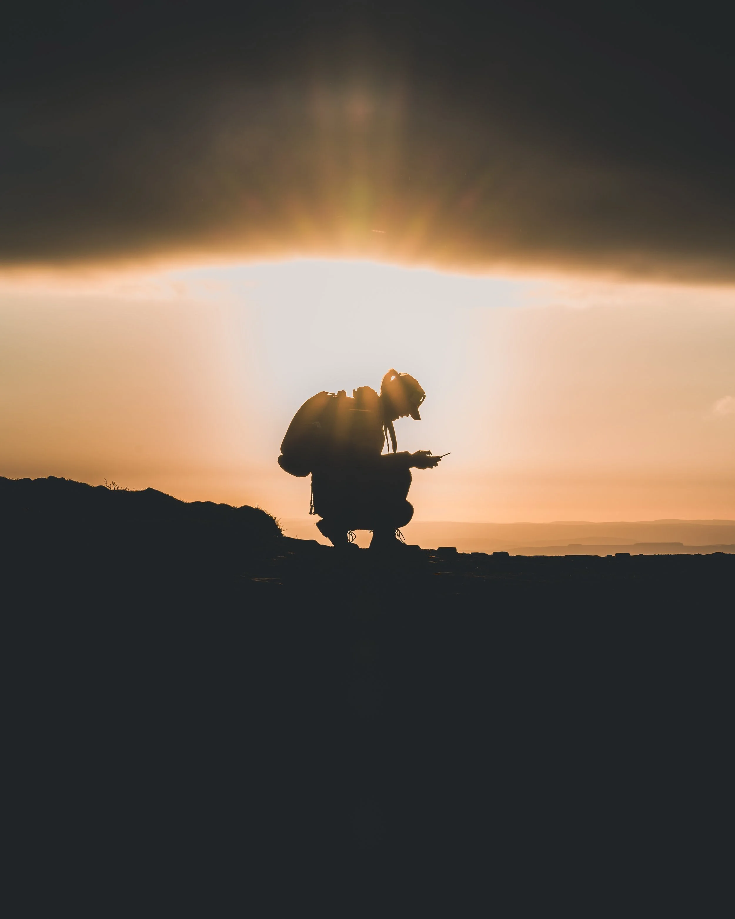 Silhouette of a hiker crouching on a summit at sunset