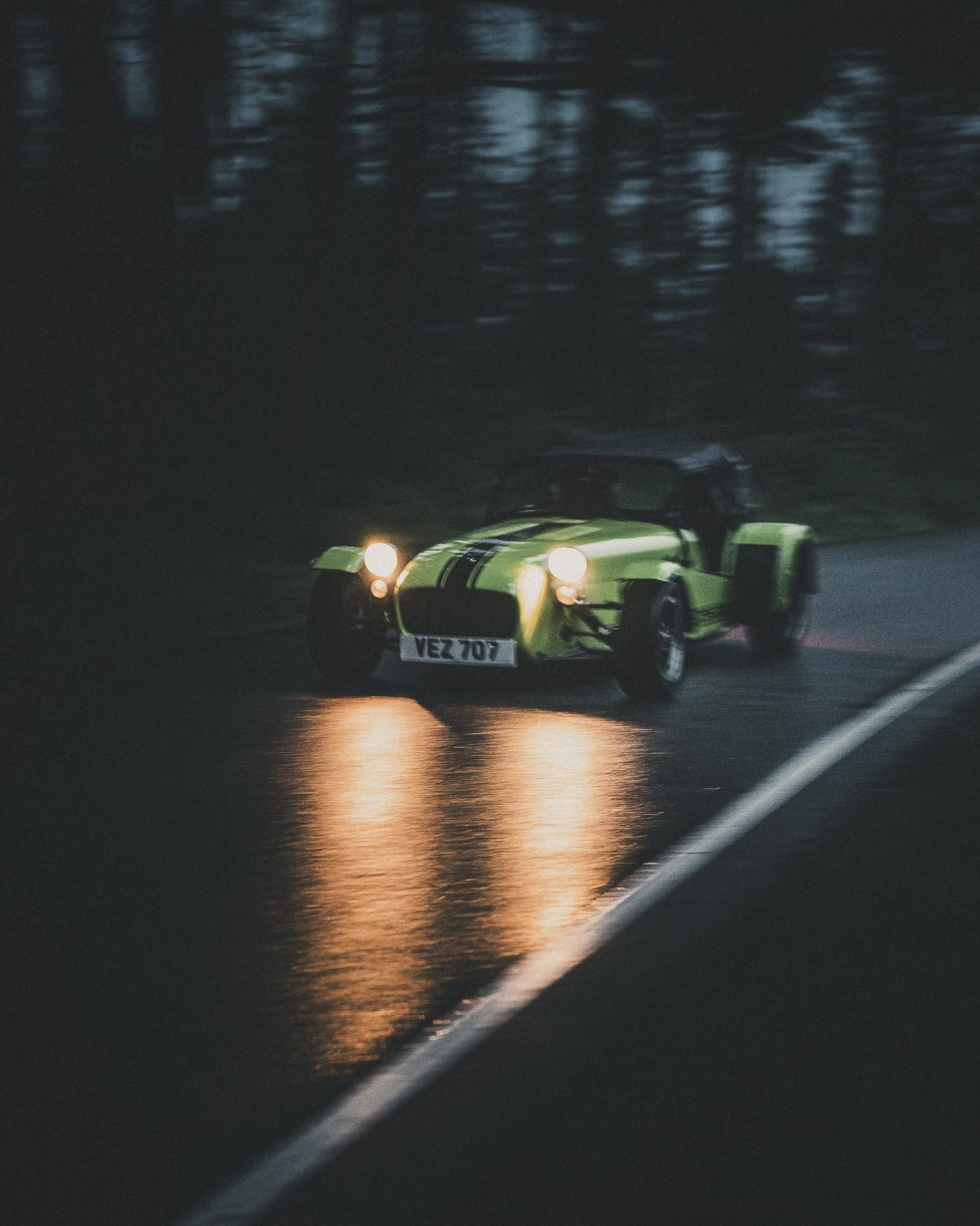 Caterham Seven with headlights on a wet road