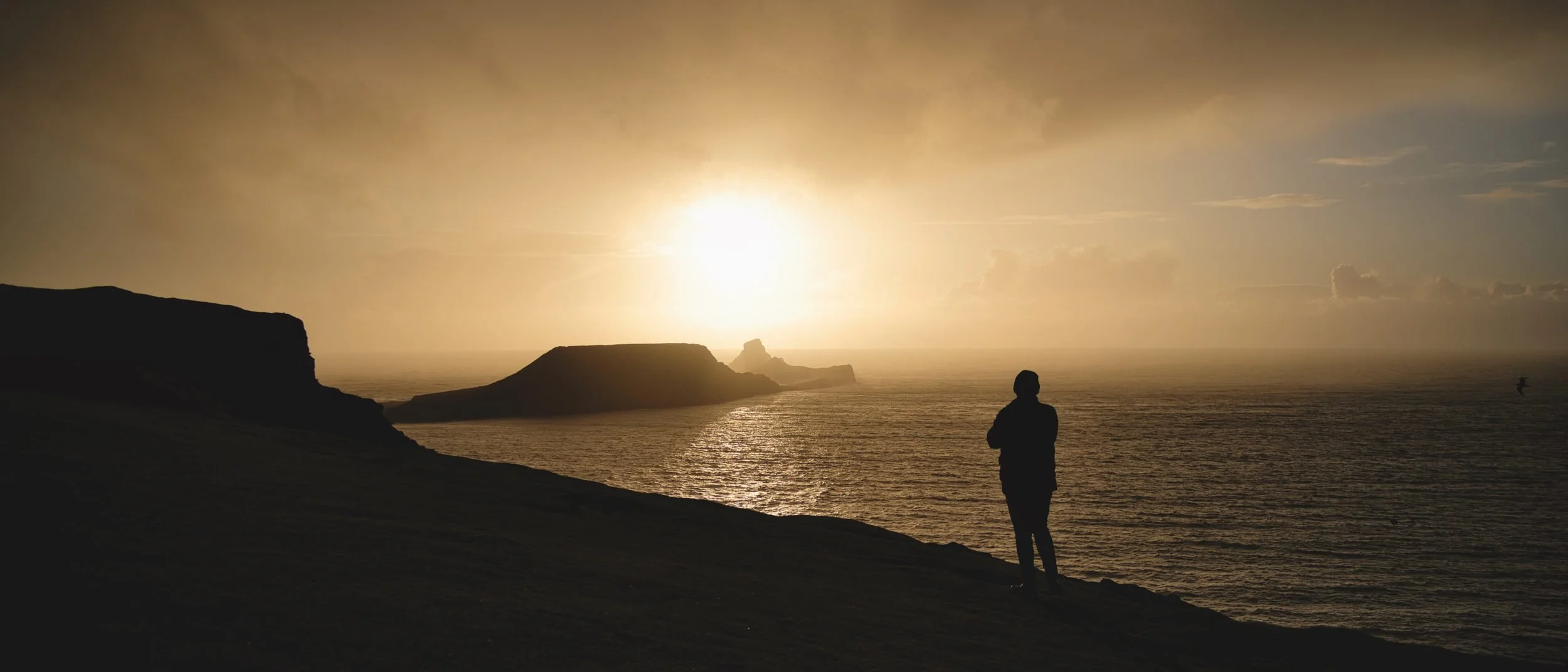 Figure watching the sun set over Worms Head, Rhossili