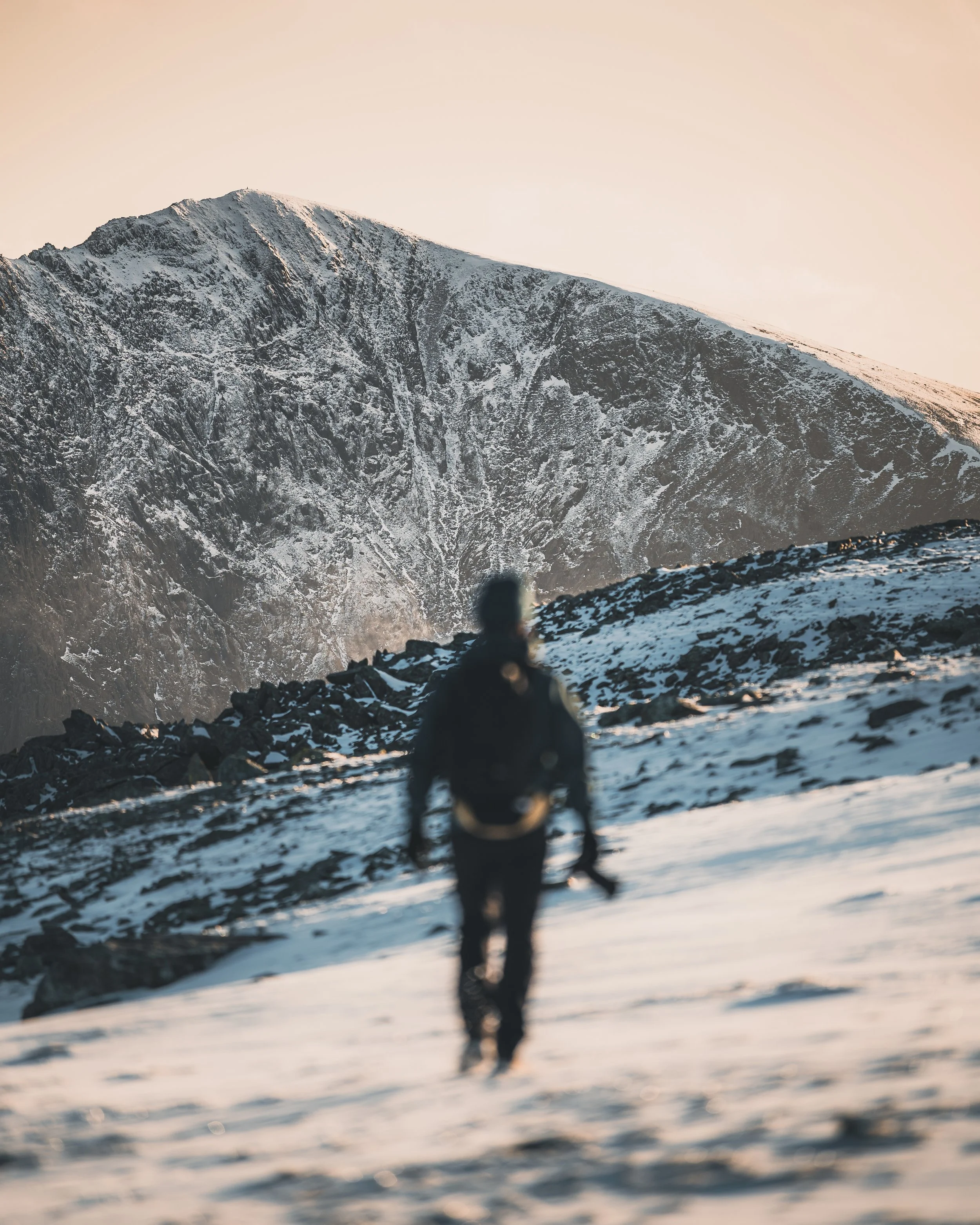 Hiker walking across snow below a mountain