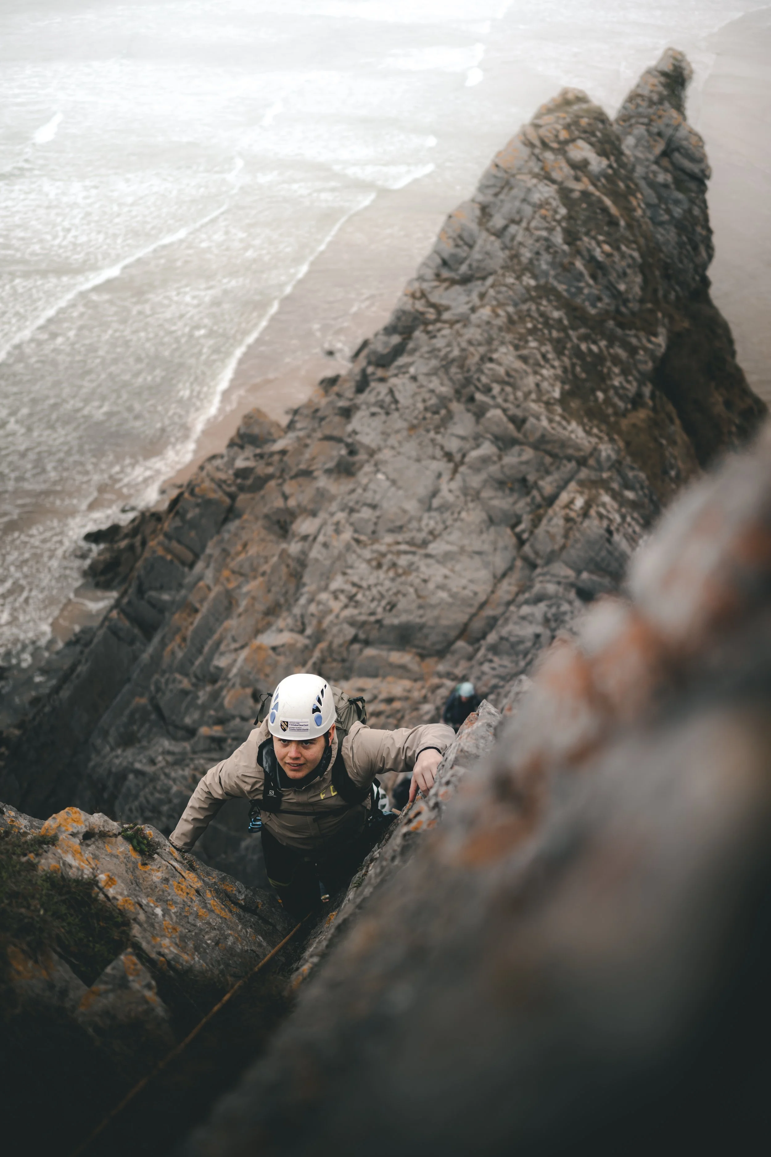 Climber scrambling up a rocky ridge above the sea