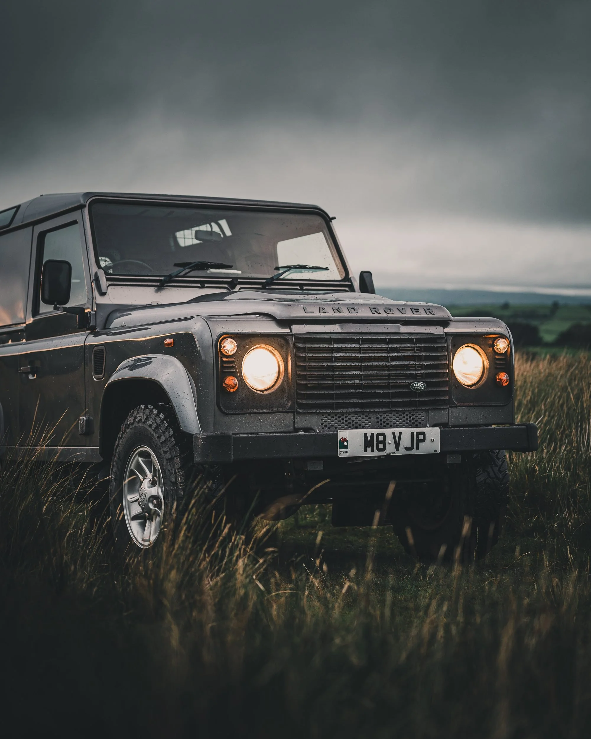 Land Rover Defender in long grass beneath dark clouds, Bannau Brycheiniog