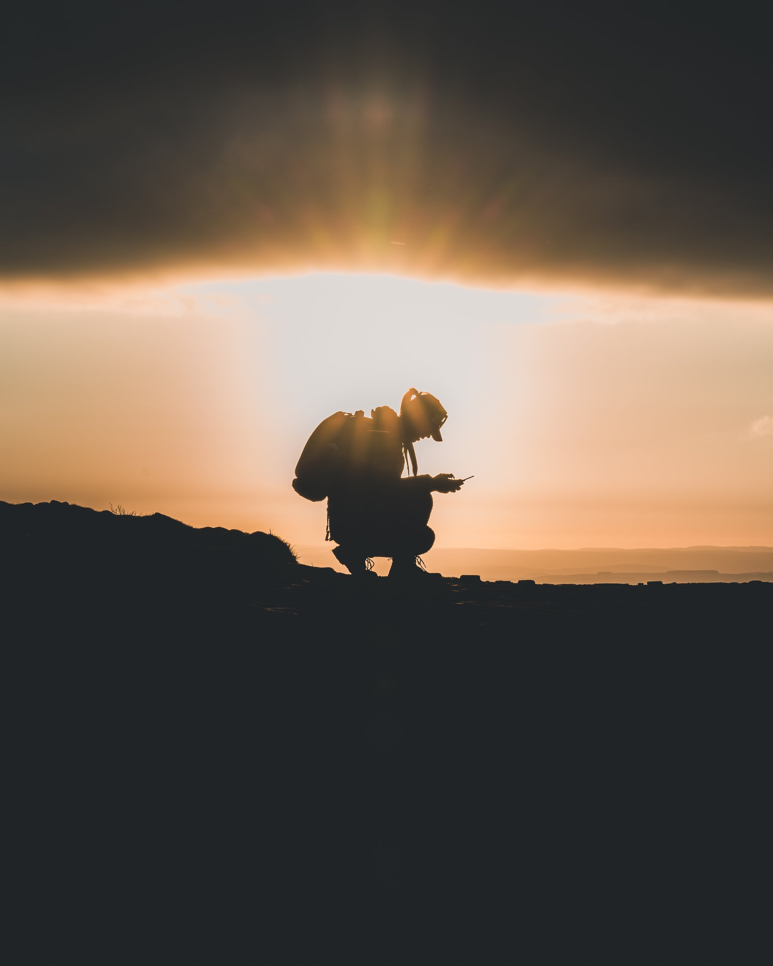 Silhouette of a hiker crouching on a summit at sunset