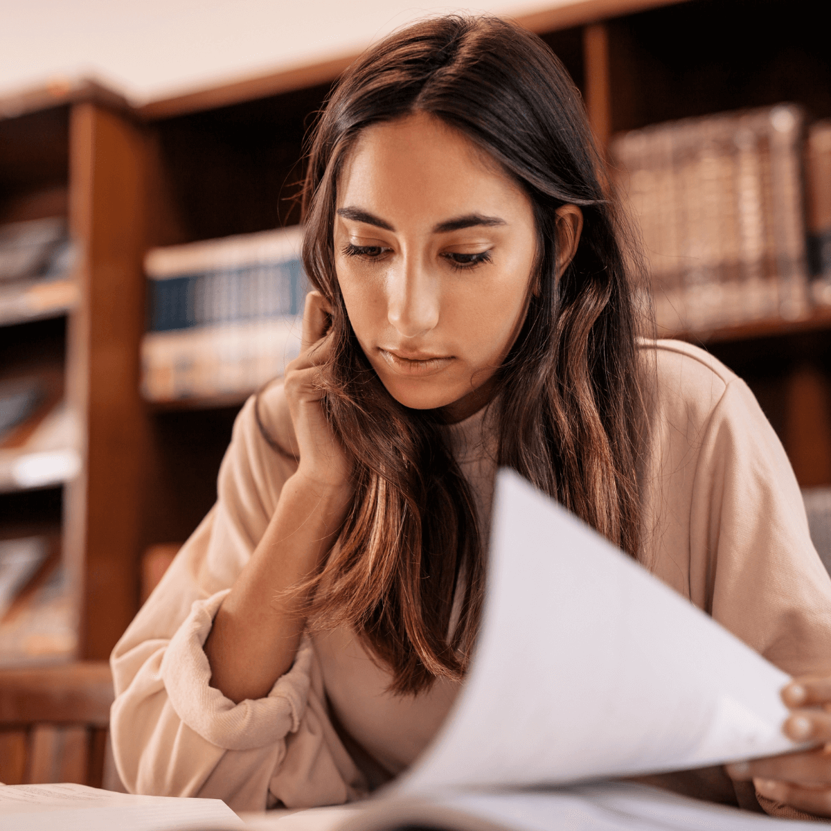 A young woman in a library reading a book or research paper