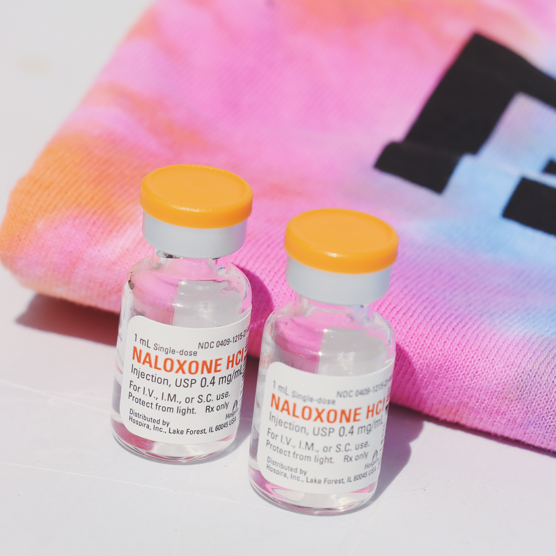 Two naloxone vials with a tie dye t-shirt folded in the background.