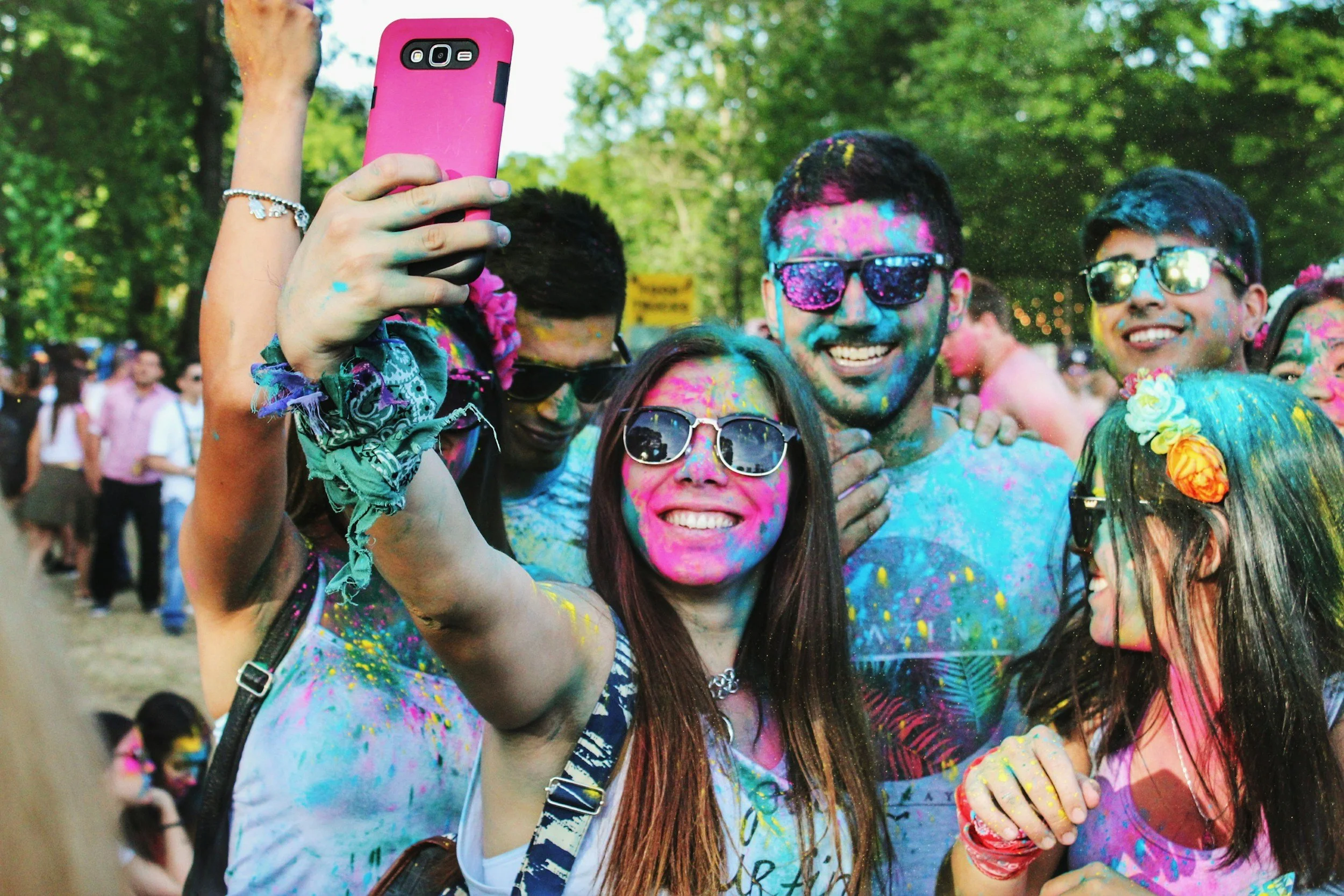 Group of people celebrating Holi with colorful powder on their faces and clothes, taking a selfie outdoors.