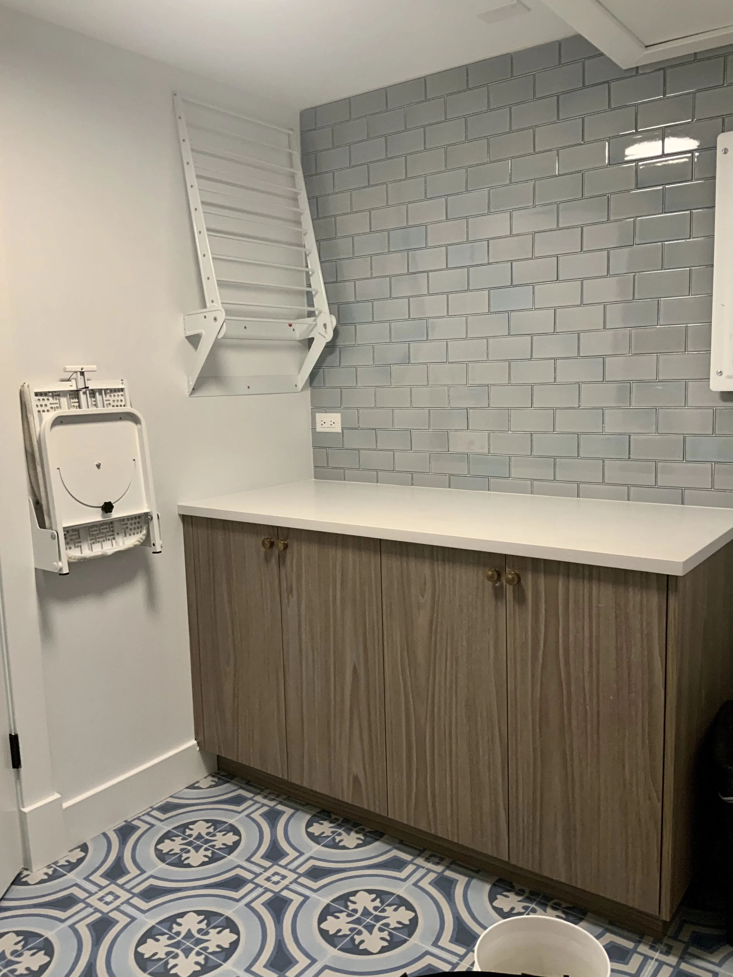 A view of the other half of the laundry room with ironing board, storage, and drying rack opposite the laundry machines. Pardon the snapshot, photography in small rooms is always a challenge. The quartz top is impervious to water, a good tip when yo…