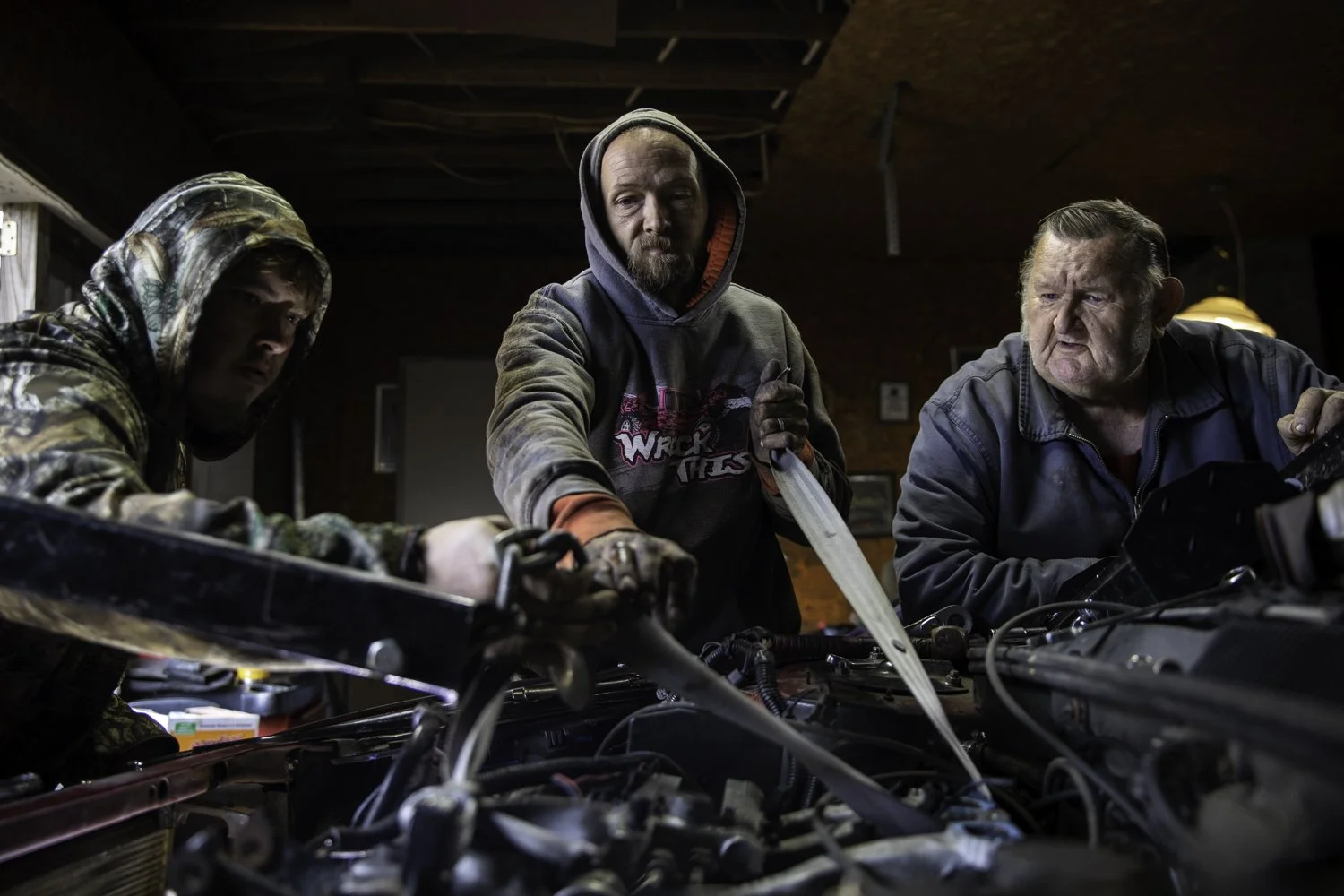 Dominick Severt, Denny Roberts, and Denzil ‘Grampa’ Roberts of New Marshfield, Ohio work together to hoist an engine out of a newly purchased car on Oct. 18, 2022. Denny Roberts bought the car from a friend for $300 and hopes to make some money by s