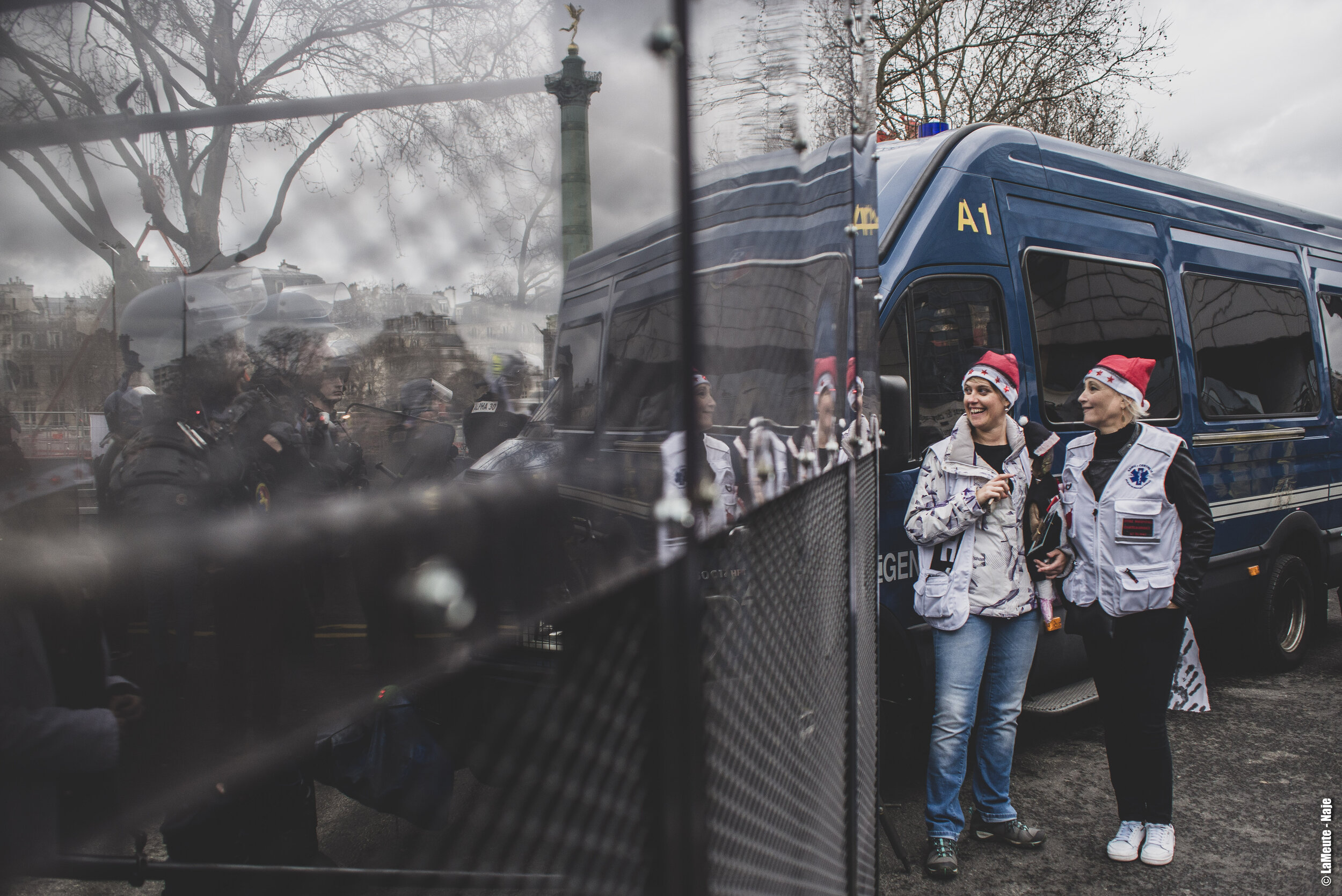   Aux abords de la place de la Bastille, les FDO ont mis en place des grilles anti-émeutes. Deux manifestant•es s’amusent d’une ligne de CRS positionnée derrière l’une d’elle.  ©LaMeute - Naje 