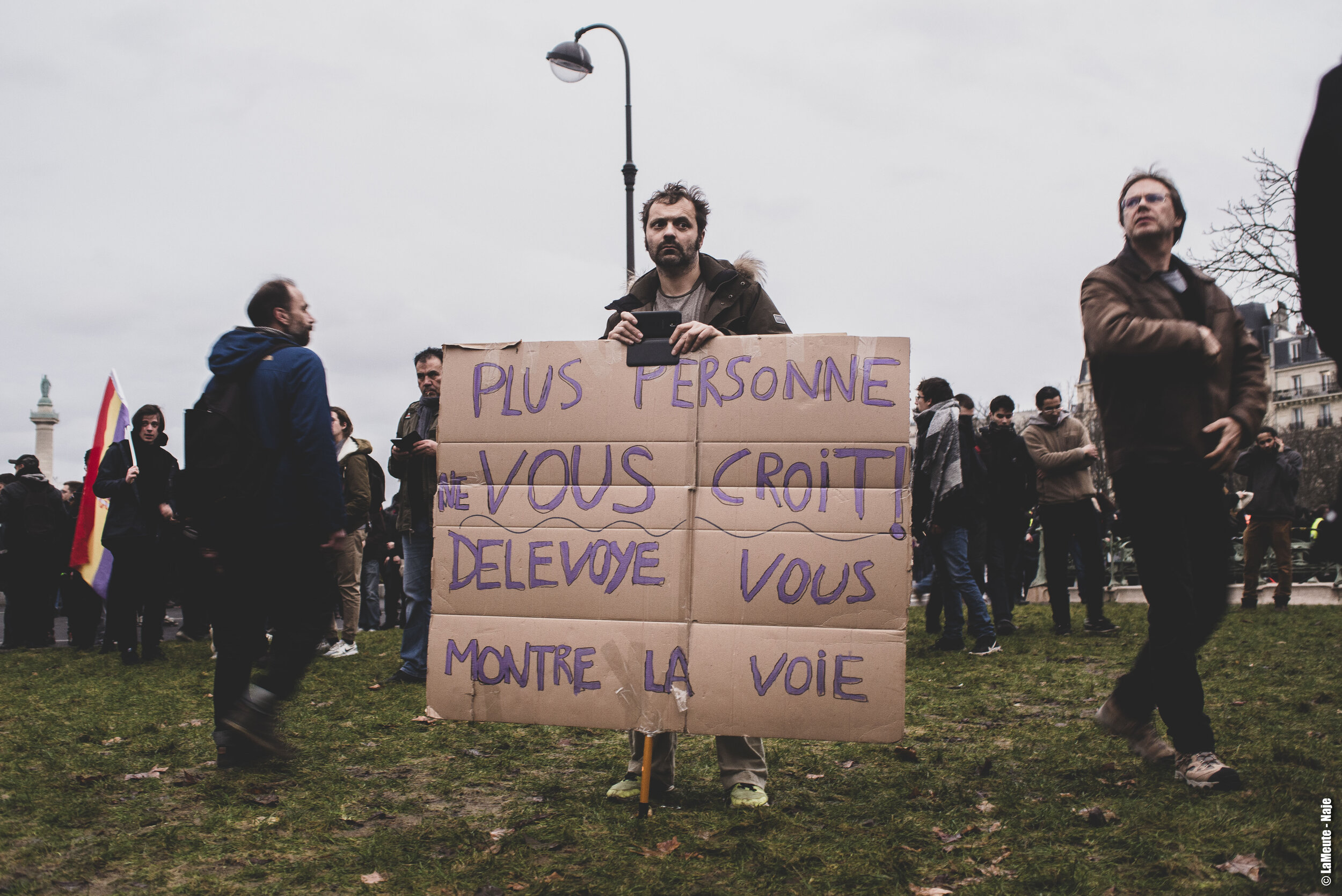   La manifestation arrive Place de la Nation. Un homme tient une pancarte sur laquelle on peut lire une invitation à suivre l’exemple de Delevoye. À qui pense-t-il?  ©LaMeute - Naje 