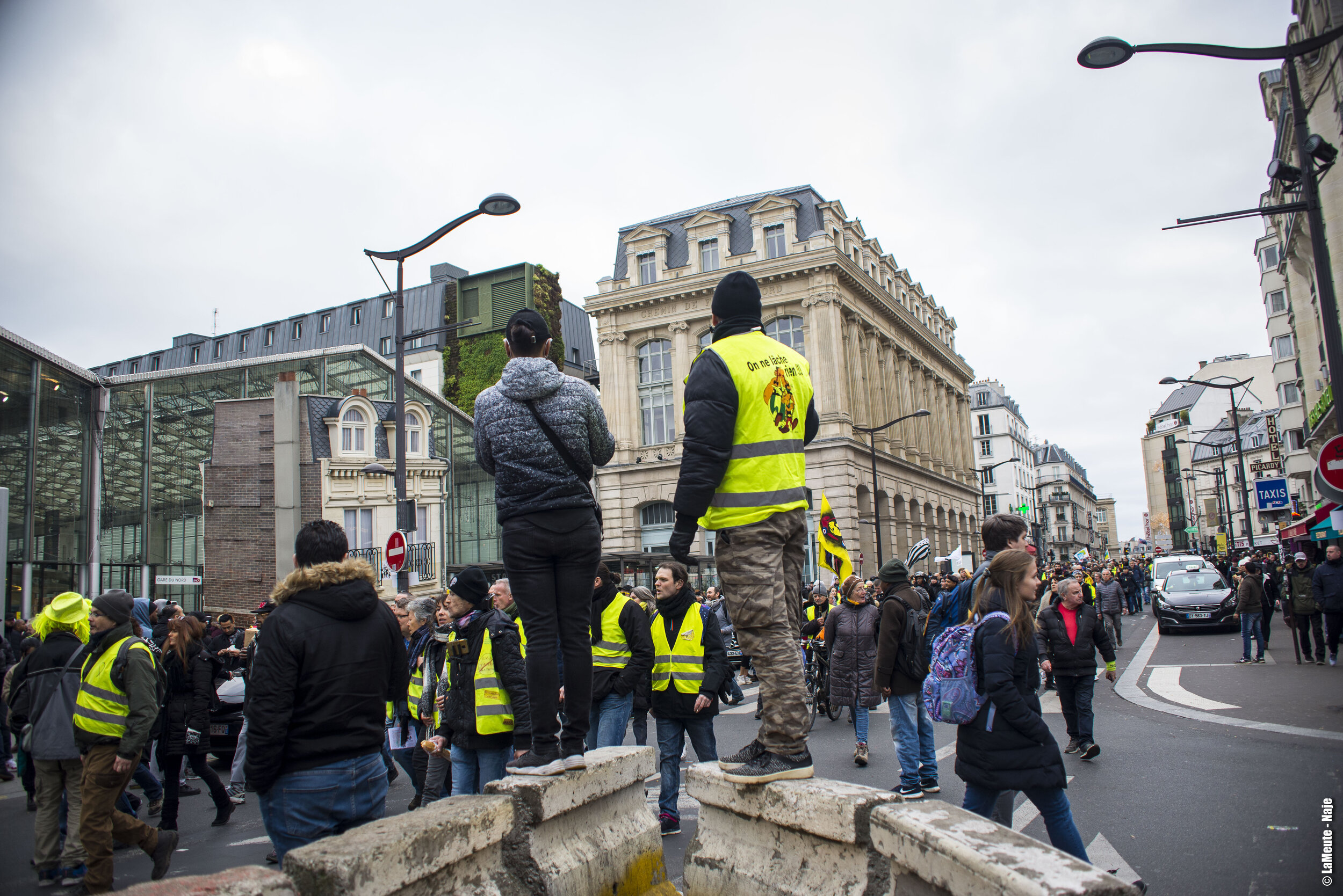   Deux manifestants prennent un peu de hauteur pour observer la foule remplir peu à peu l’esplanade face à la gare.  ©LaMeute - Naje.      