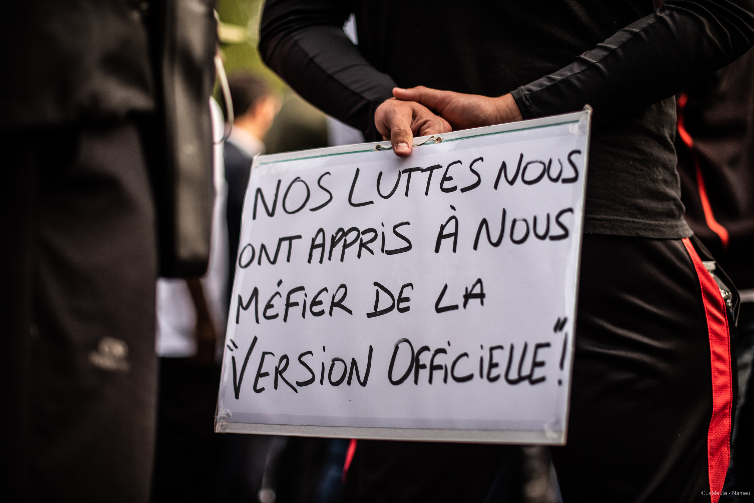   Une personne venue apporter sa solidarité à la famille de Ibrahima porte une pancarte où l’on peut lire « Nos luttes nous ont appris à nous méfier de la « version officielle ».  © LaMeute -Nameu- 