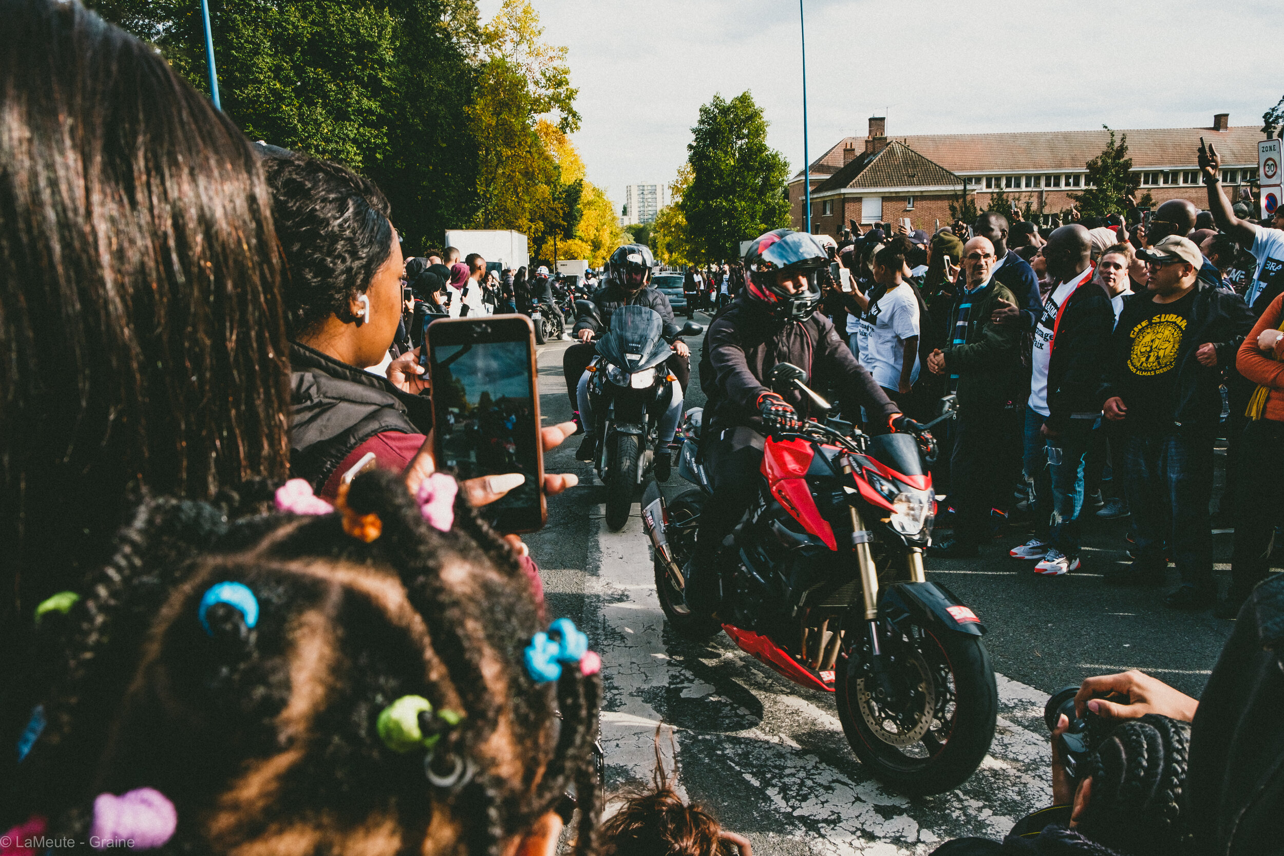   À l'endroit même où Ibrahima est mort à moto, les jeunes du quartier font une haie d'honneur à d'autres motards qui défilent dans le quartier. Le moment est fort en symbolique.  © LaMeute -Graine- 
