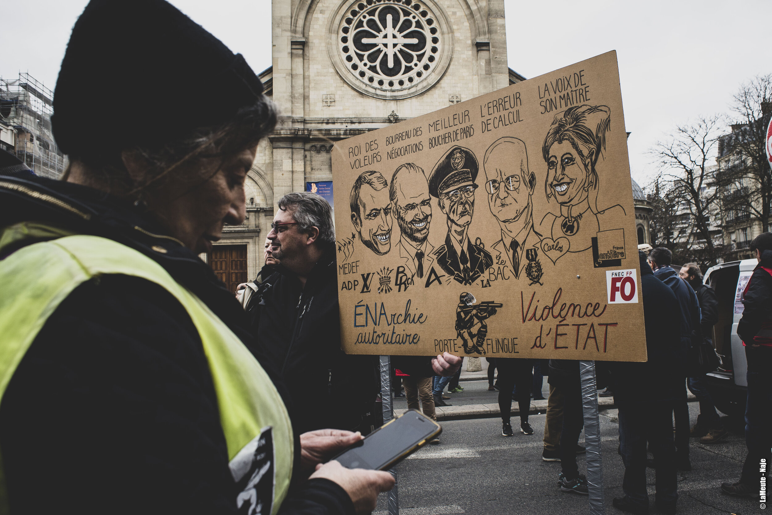   Une femme Gilet Jaune vient de prendre en photo ce panneau illustrant les protagonistes d’une «&nbsp;Énarchie autoritaire&nbsp;».  ©LaMeute - Naje 