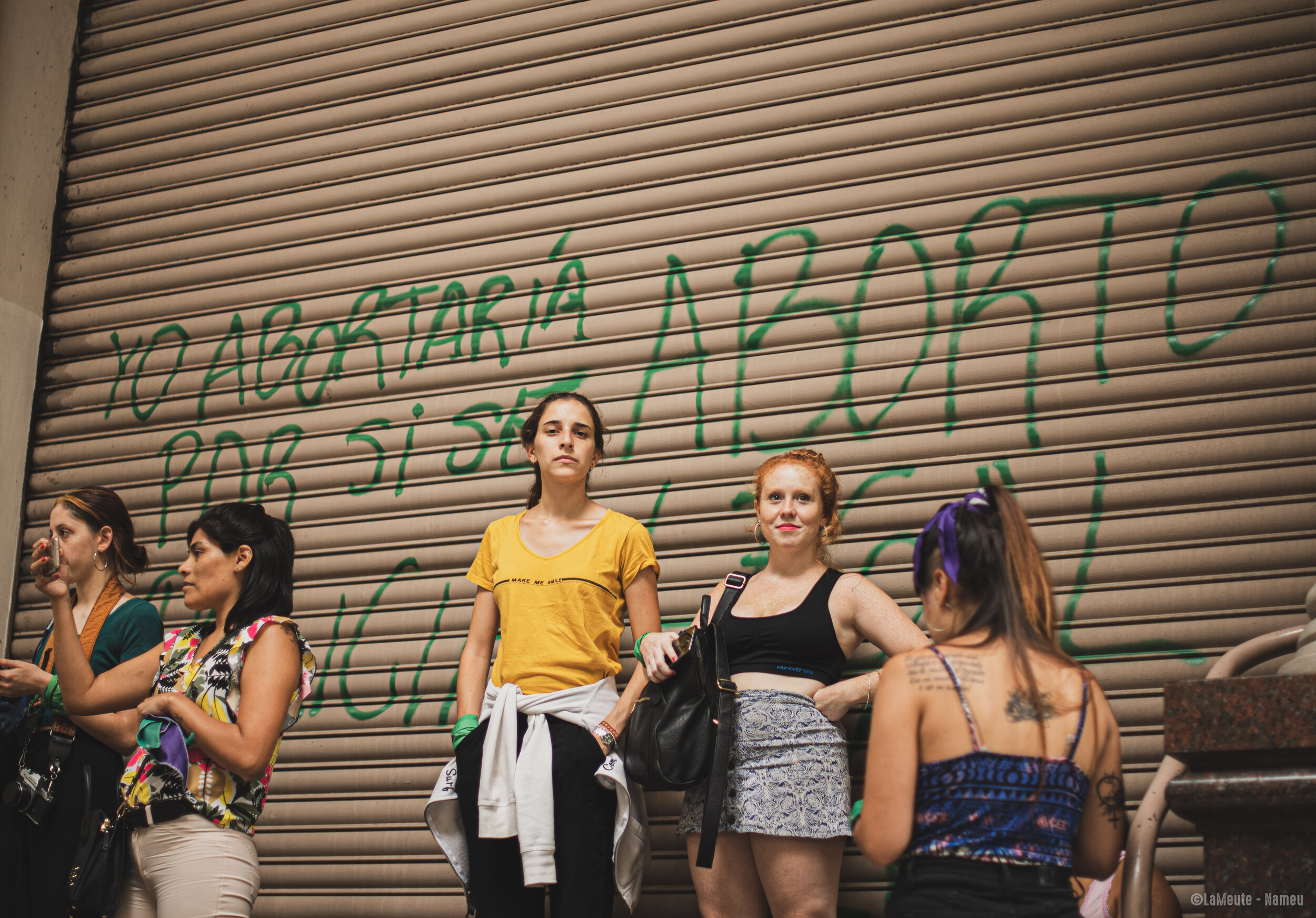   Des manifestantes regardent le cortège avancer, derrière elles un graffiti dit : « Je préférerai avorter que de prendre le risque qu'il devienne policier ». L'avortement est illégal en Argentine sauf quand la vie de la mère est en danger ou lorsque