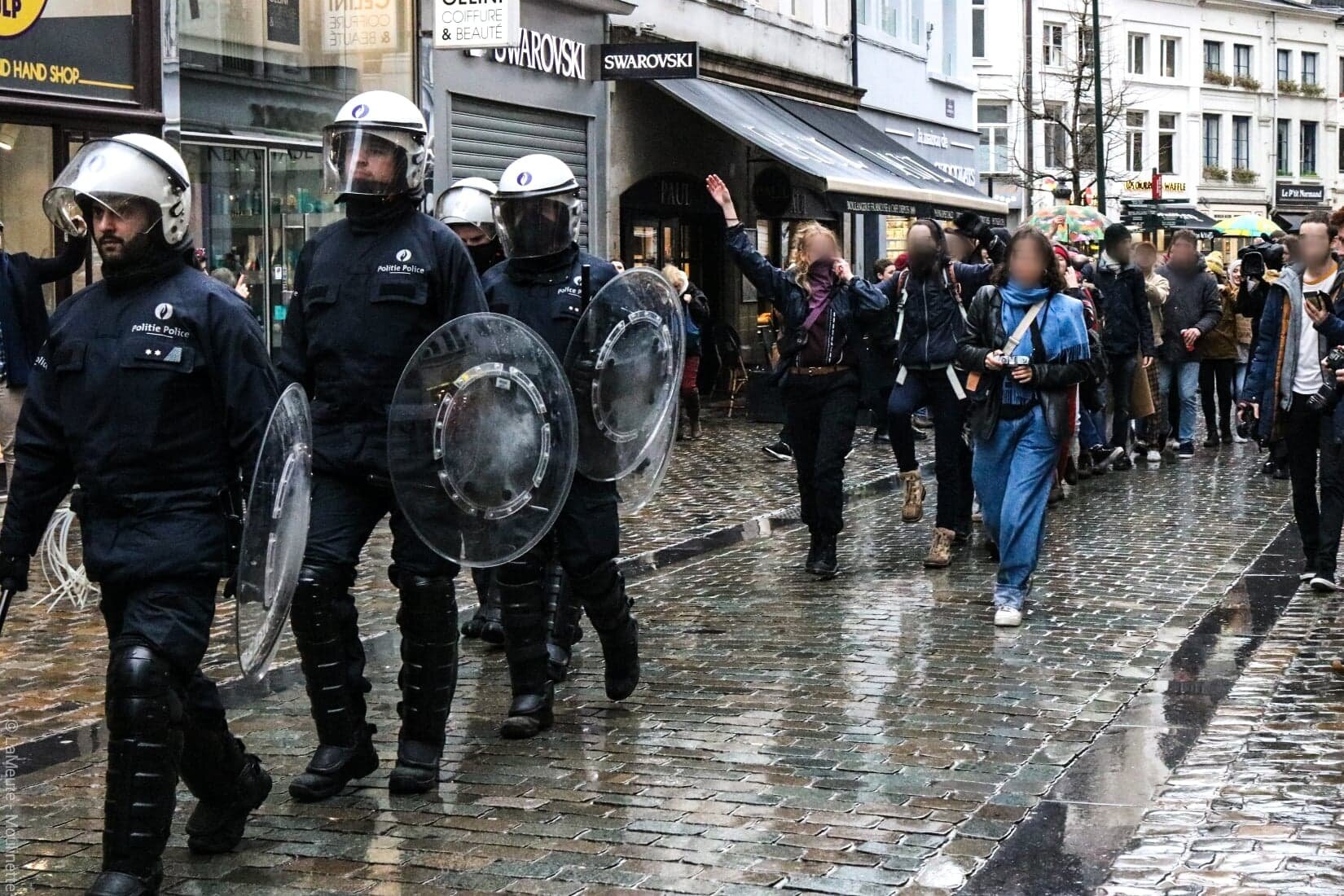   Les policiers errent dans le centre-ville de Bruxelles à la recherche des responsables des manifestations sauvages qui se sont déclarées plus tôt. Ils sont rapidement suivis par des manifestantes qui chantent et font la chenille derrière eux. Certa