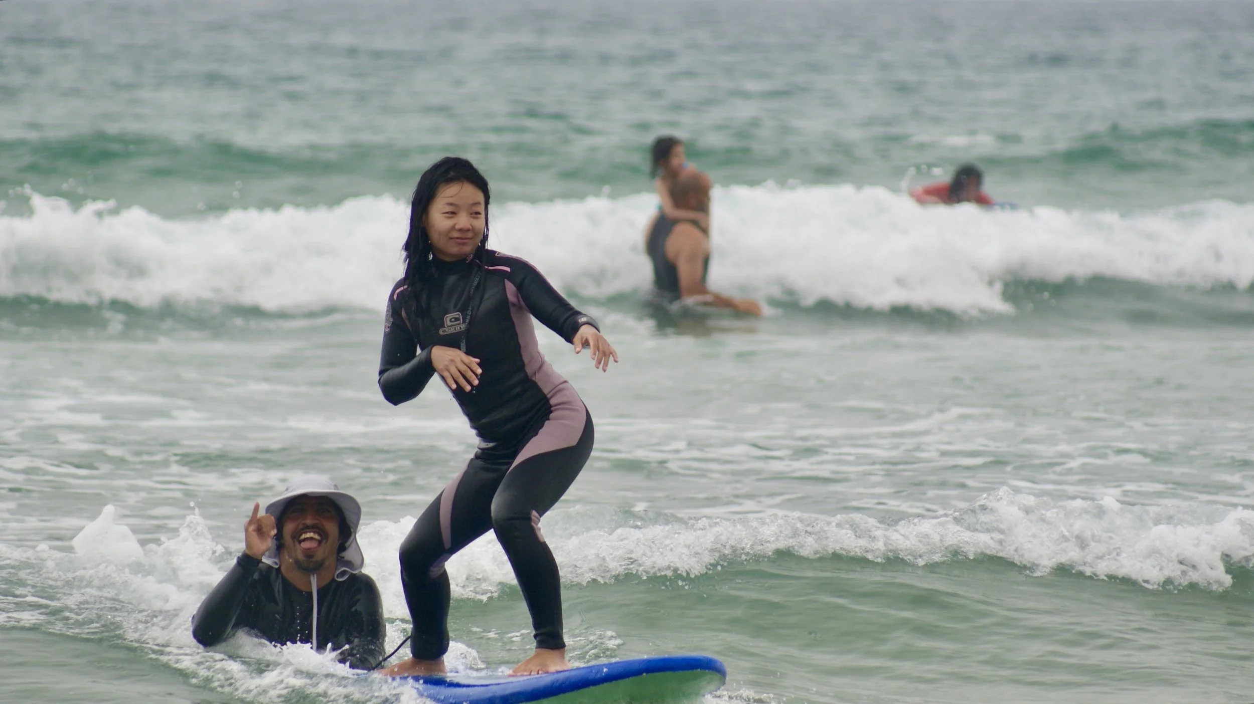 Rachid Makoua, ISA surf coach, head surf coach of Local Surf Maroc helping a beginner surfer catch waves by stabilizing her board.
