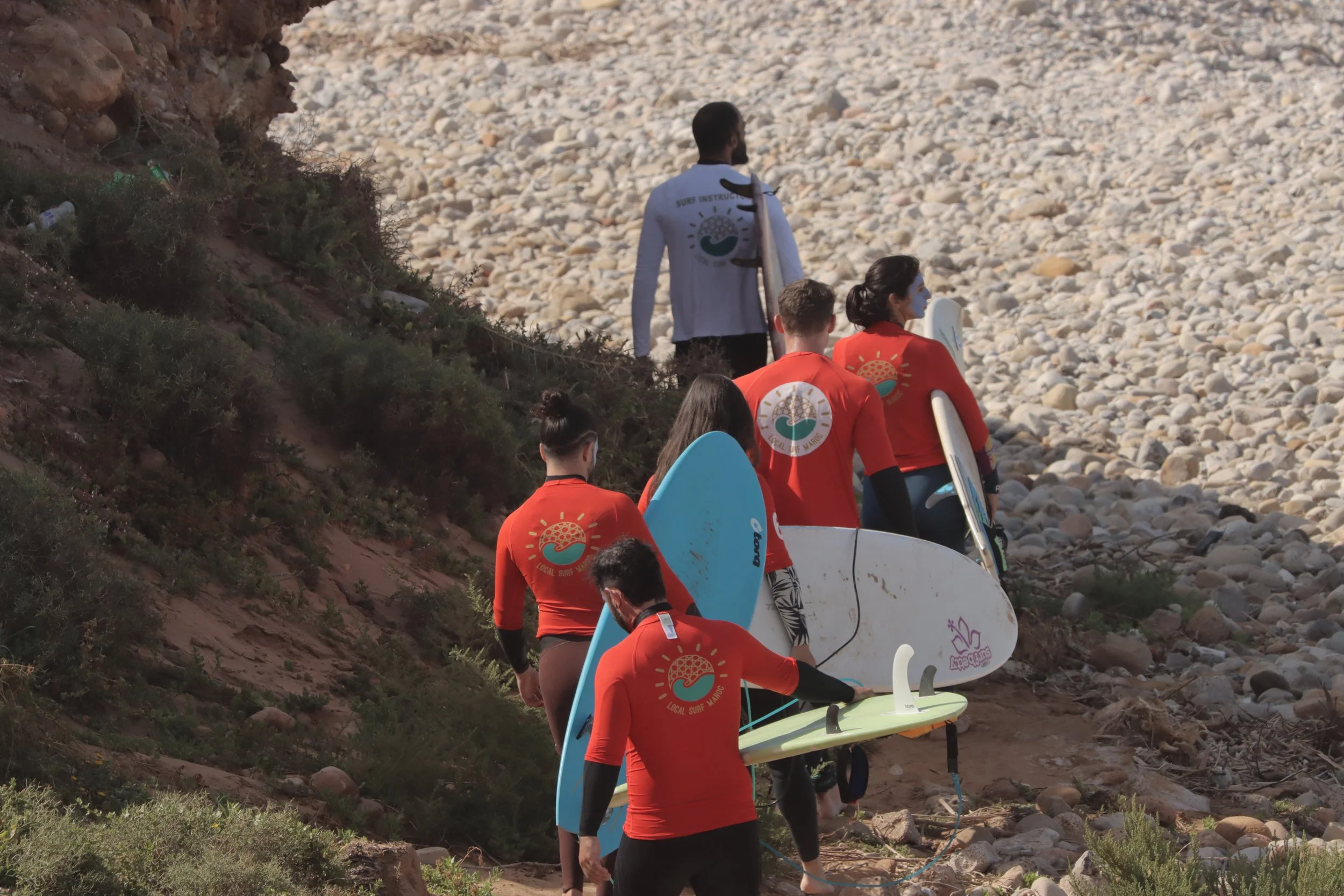 Advanced Intermediate surfers being led by Local Surf Maroc coach, carrying surfboards, ready to paddle out at K12, Aourir, Taghazout Bay, Morocco.