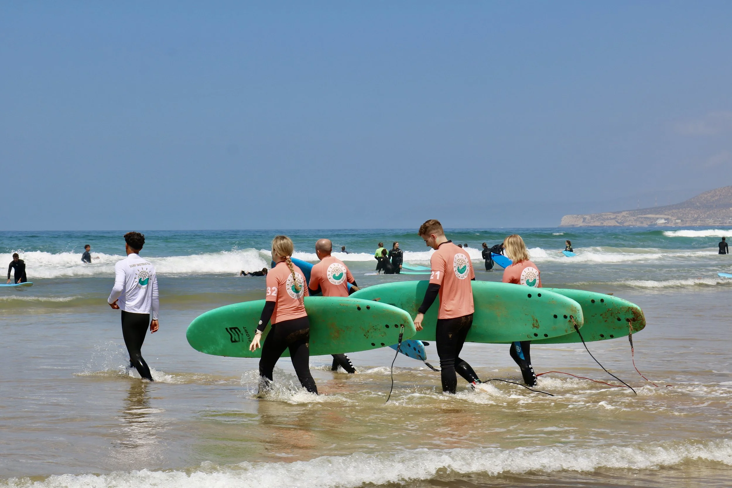 Small group of beginners surfers learning how to surf in small waves in Tamraght, Morocco