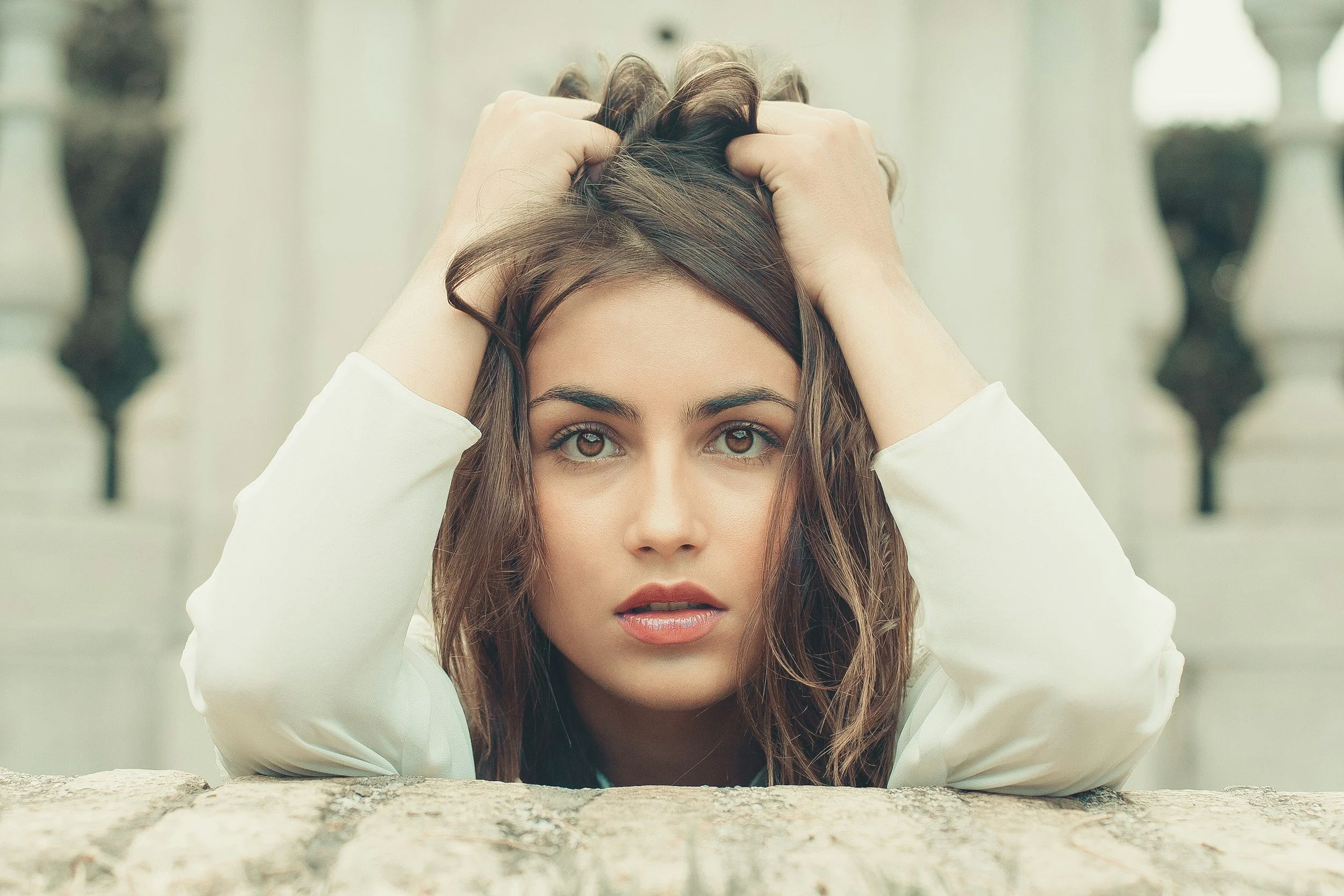 Woman with elbows on counter in a white shirt, bunching her brown hair in fits, looking overwhelmed