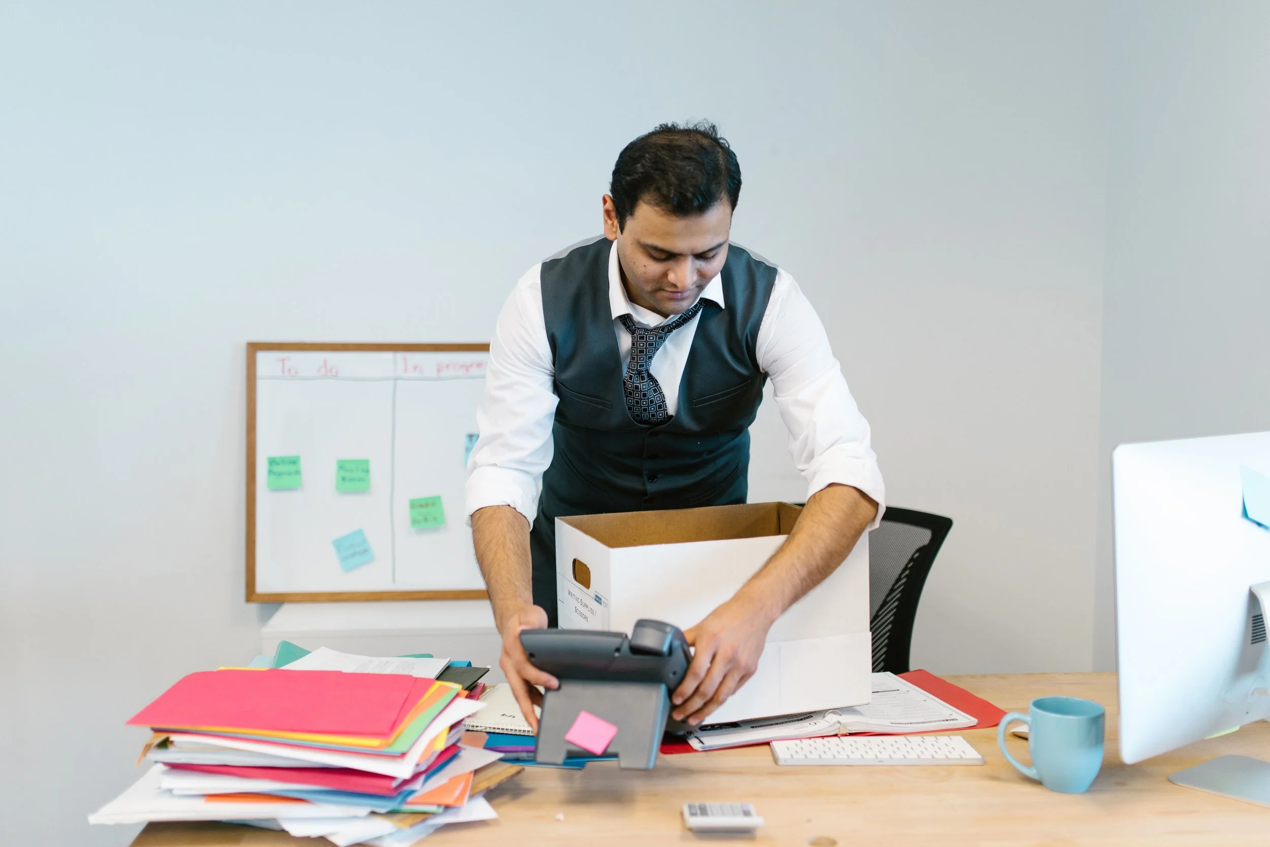 A man in a suit packing up his office supplies into a white cardboard box.