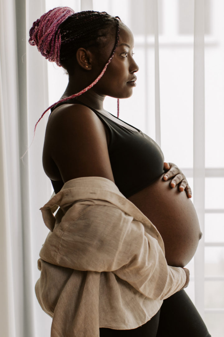 Pregnant woman with pink braided hair looking out a window.