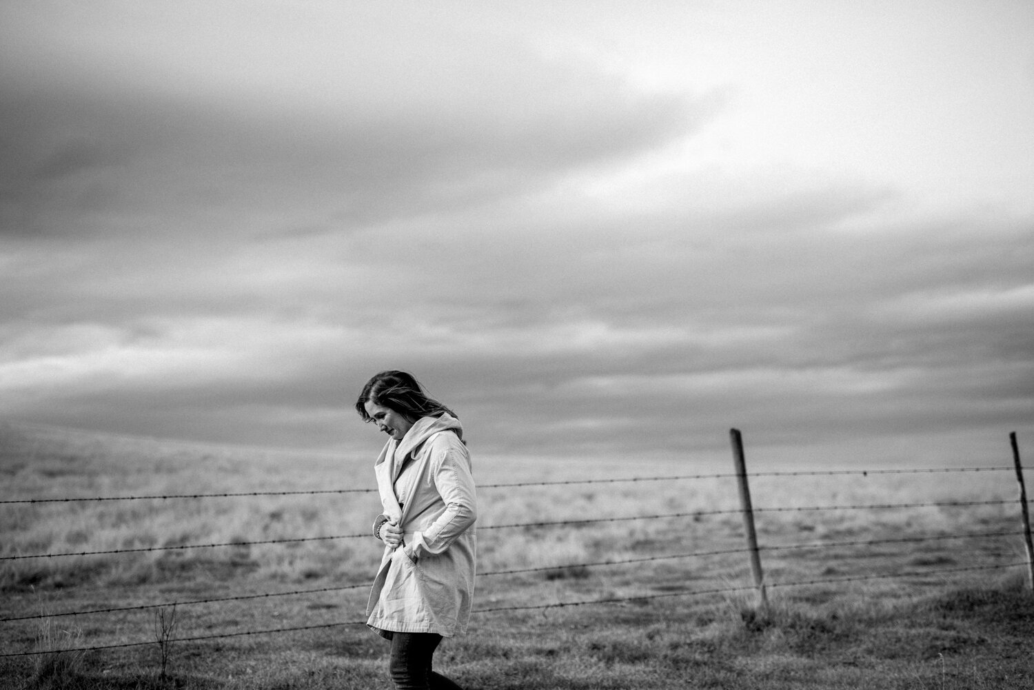  kathryn learie commercial pet photographer walks through the kamloops landscape with hands in her jacket pockets looking down and smiling 