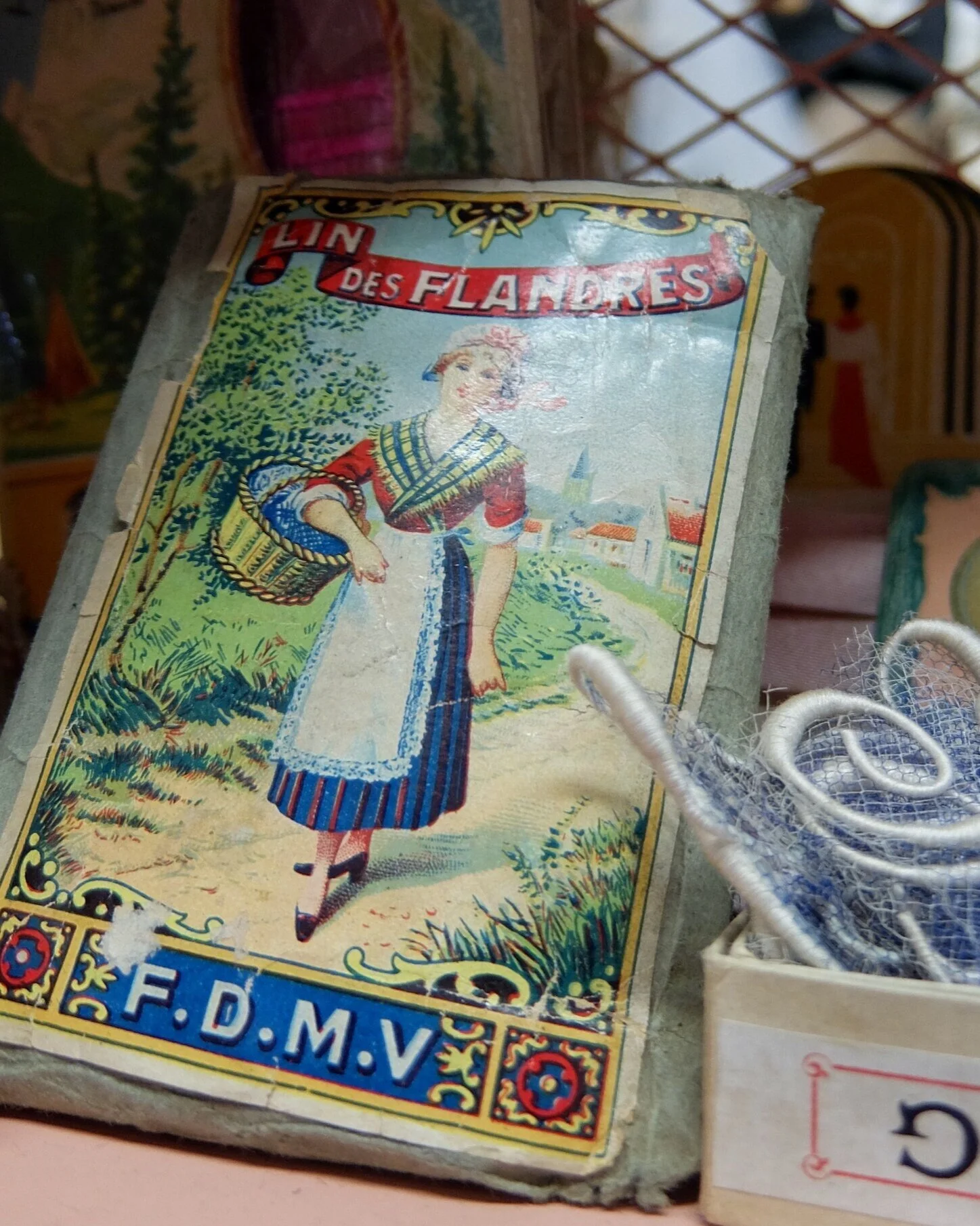 Vintage illustrated matchbox cover featuring a woman in traditional dress walking along a rural path with houses and trees in the background.