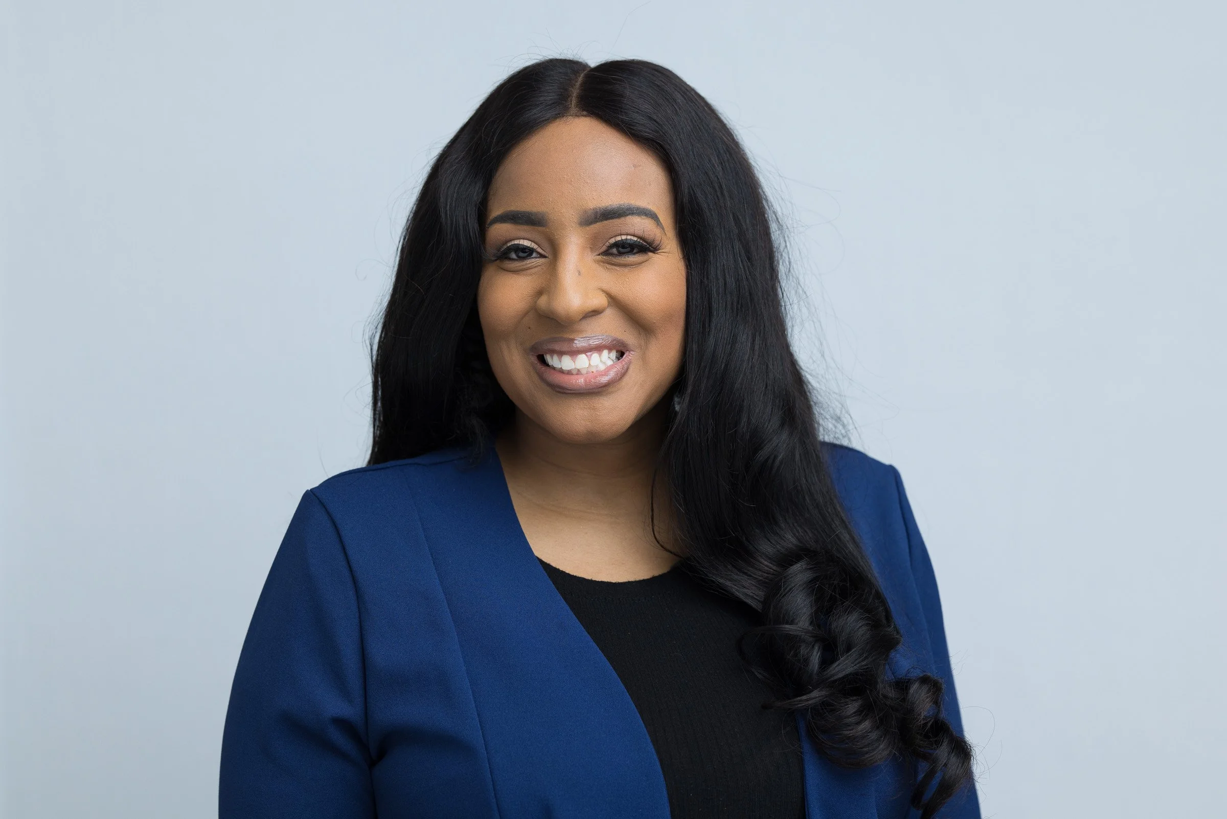 Kiyana has long black hair and is wearing a blue blazer with a black blouse.