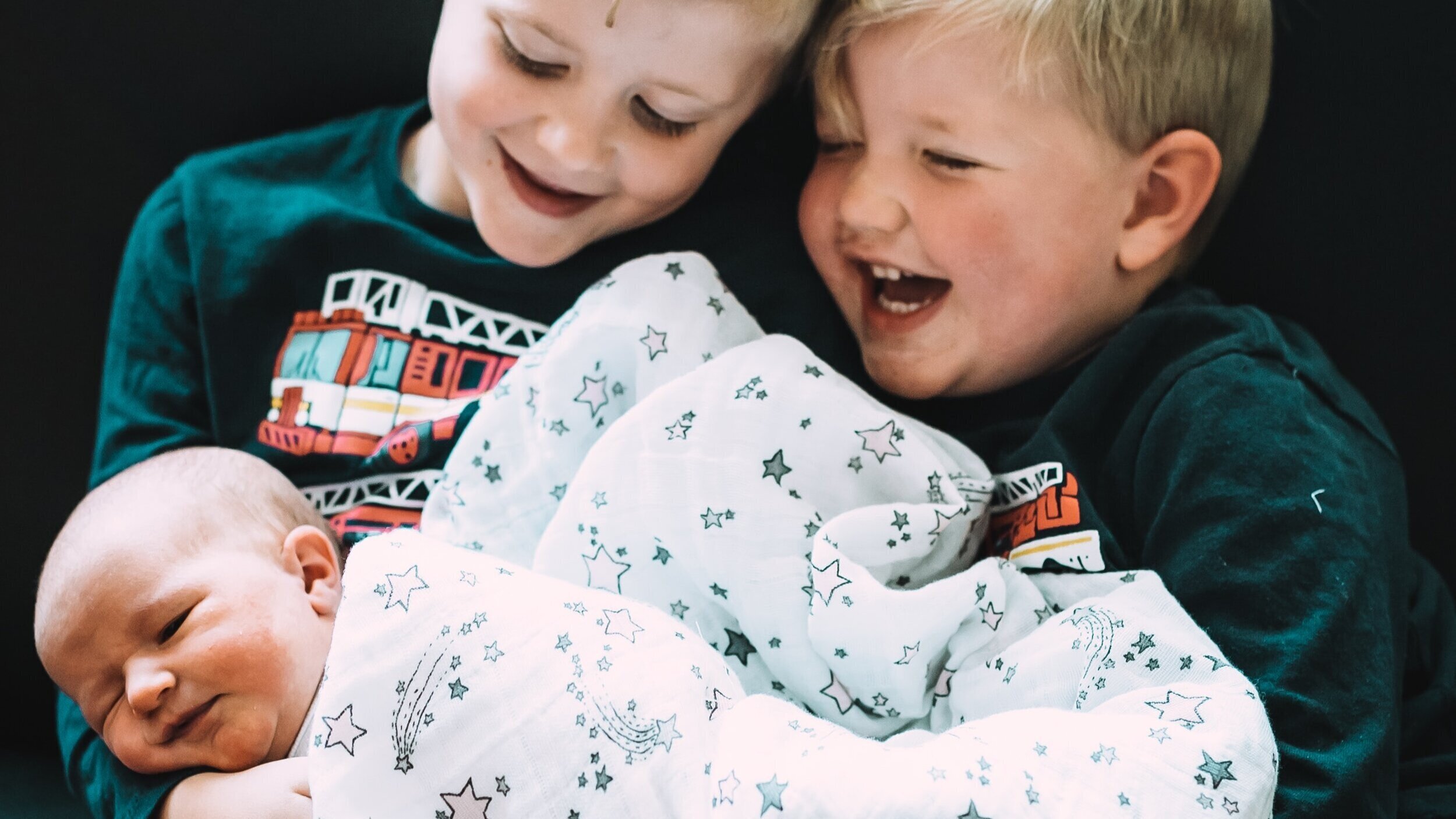  Photo of two happy little boys holding their baby brother. 