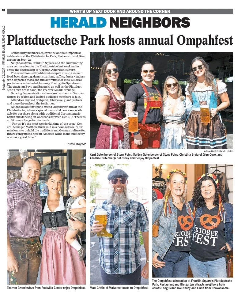 Four women in traditional German dirndl dresses holding beer mugs, smiling at an outdoor Oktoberfest celebration. Women wearing sunglasses are in the foreground, with festive decorations visible behind them.