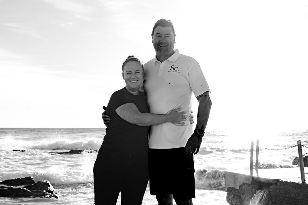 A smiling couple hugging on the beach with ocean waves in the background, black and white
