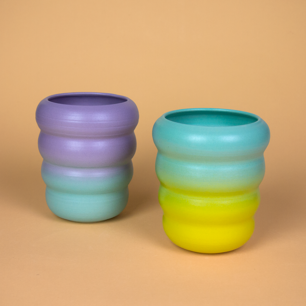 two handmade ceramic cups with wavy designs and colorful gradient glazes.