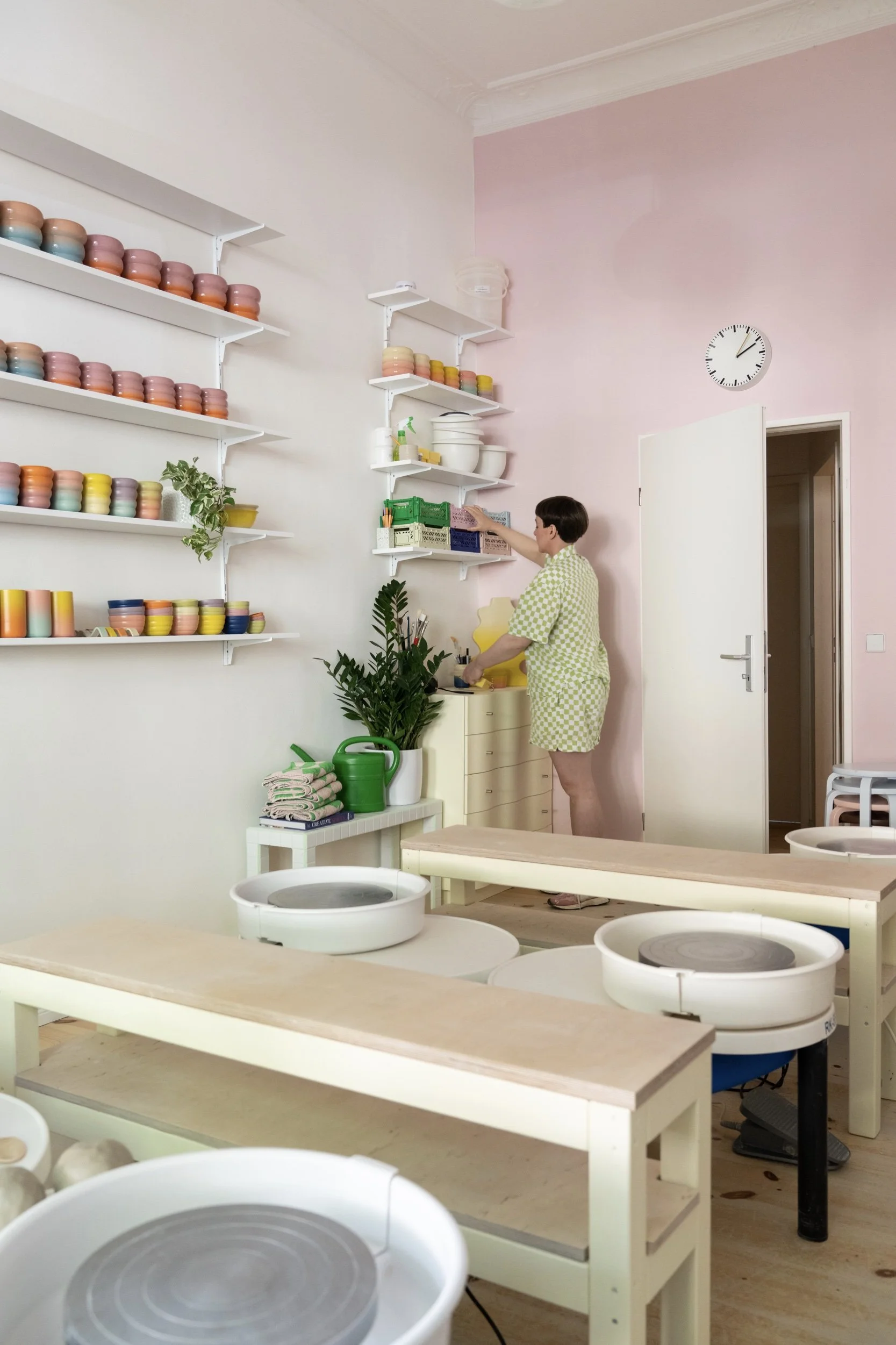 Marilyne Blais steht in ihrem Keramikstudio und ordnet Regale voller buntem Geschirr.