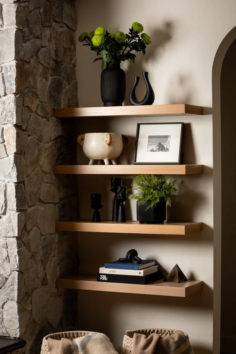 Luxury interior design by Design Bar Bend in Bend, Oregon for the ParkHaus project featuring natural wood floating shelves styled with black ceramic vases, sculptural objects, curated coffee table books, and greenery against an arched wall detail and