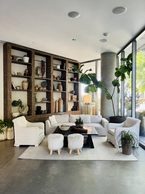 A seating area with white couches and chairs sits in front of styled wooden shelves in the 1 West Hollywood Hotel.