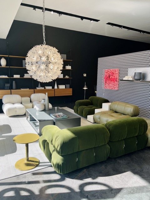 A round chandelier hangs atop a modern living room arrangement with green and white sofas and a coffee table at West Hollywood Design District.