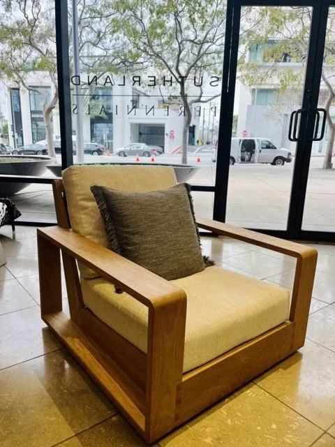 An outdoor chair with white cushions and a gray throw pillow sits with the Perennials and Sutherland sign in the back window.