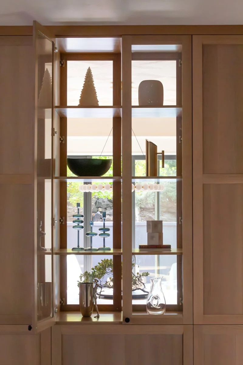 Luxury interior design detail by Design Bar Bend in Bend, Oregon for the ParkHaus project featuring a wood glass-front display cabinet styled with ceramic objects, glass candleholders, decorative vessels, and a bonsai arrangement with views outdoors