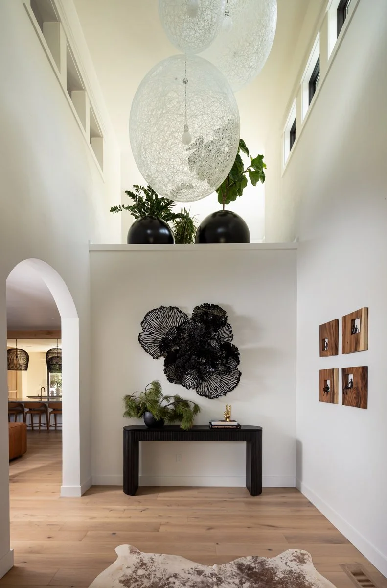 Luxury entryway interior design by Design Bar Bend in Bend, Oregon for the ParkHaus project featuring a double-height foyer with globe pendant lighting, black console table, wood block wall art panels, arched doorway, and views through to the kitchen
