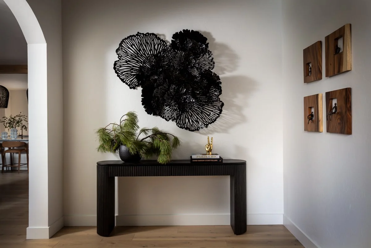 Luxury entryway interior design by Design Bar Bend in Bend, Oregon for the ParkHaus project featuring a fluted black console table, large-scale black sculptural wall art, gold accent decor, arched doorway, and wood block wall art panels with light ha